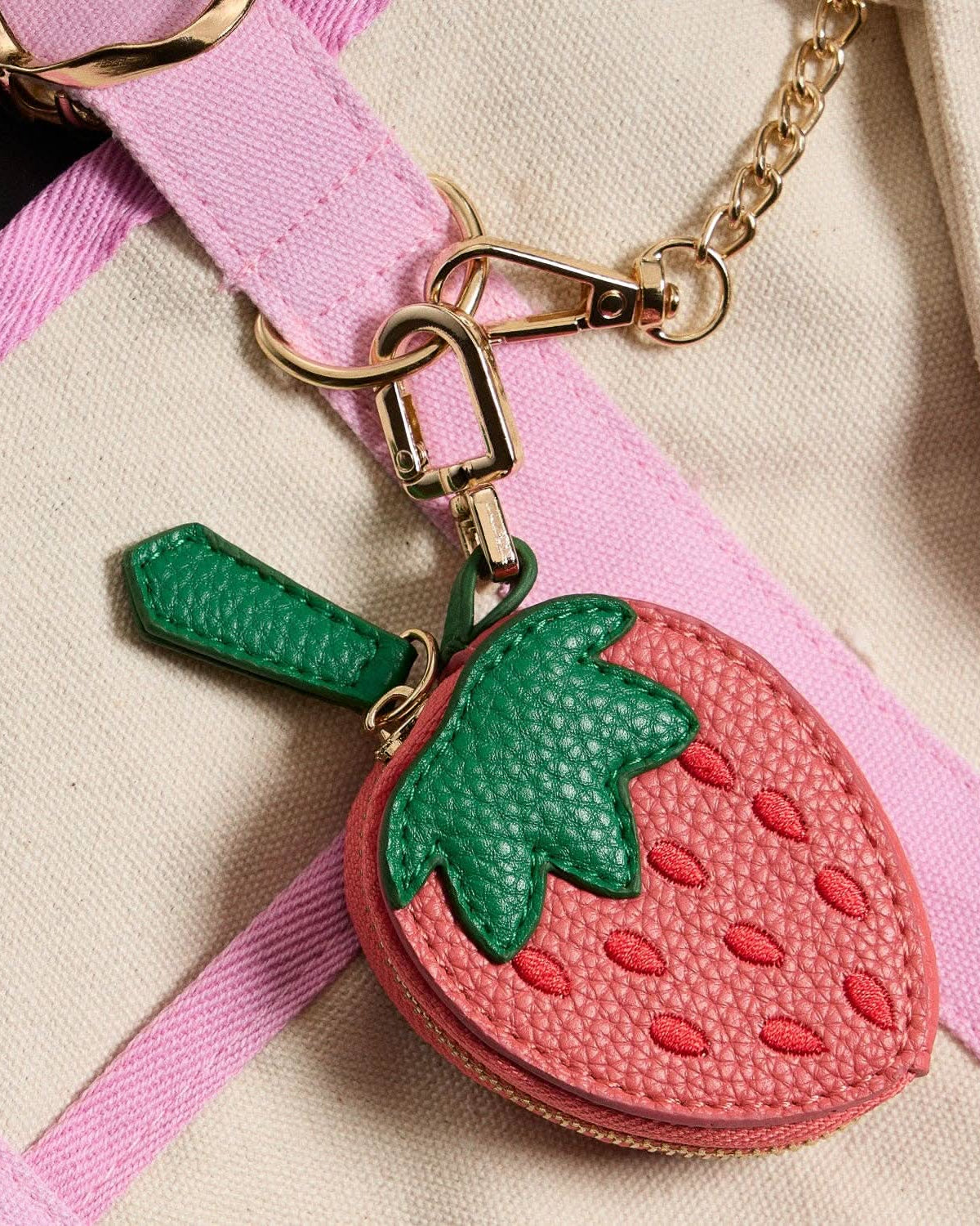 Strawberry-shaped keychain attached to a pink strap on a beige background