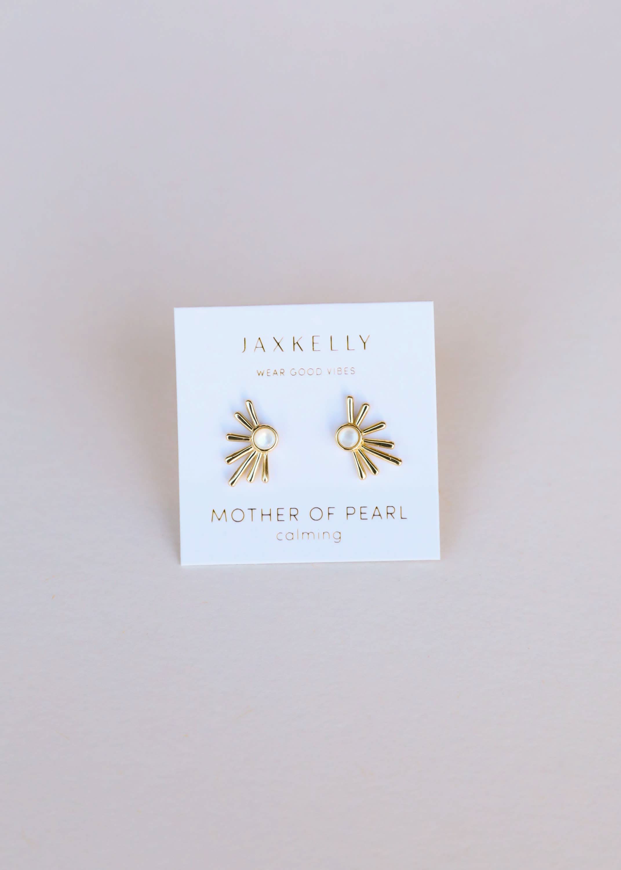 Gold earrings on a Jax Kelley branded card with a beige background