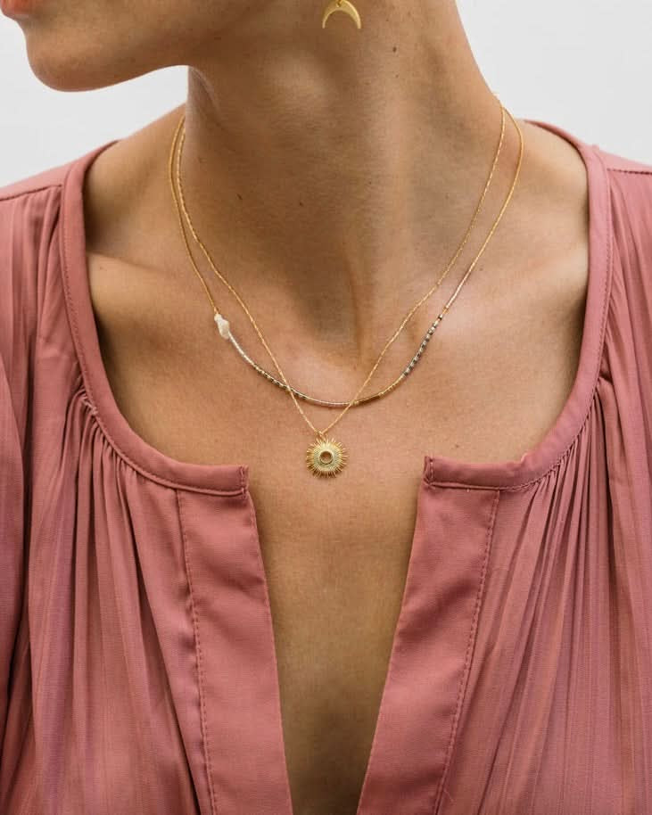 Person wearing a gold necklace with a pink top