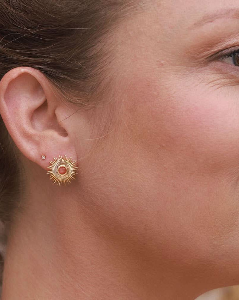 Woman wearing gold stud earrings in a circle sunburst pattern