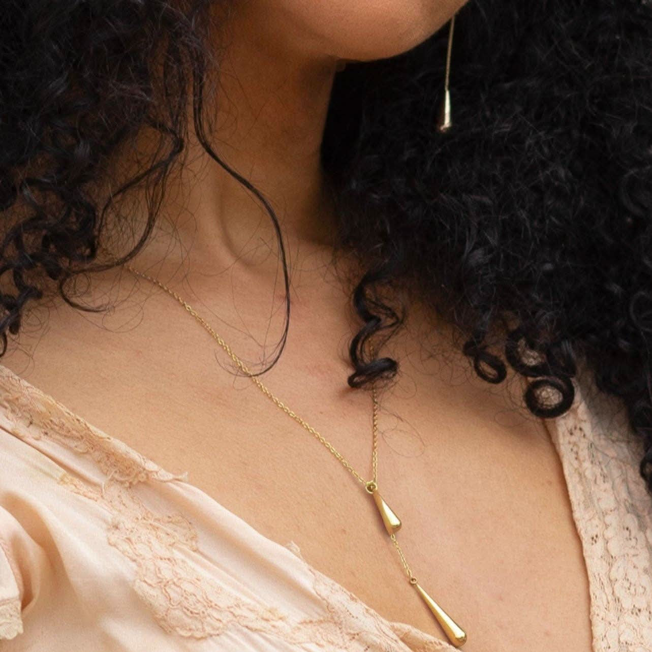 Close-up of a person wearing a delicate gold necklace with a beige top.