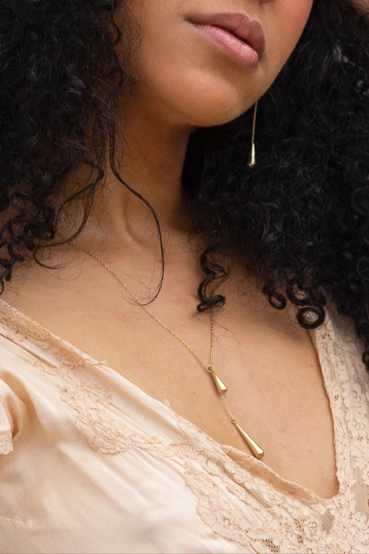 Close-up of a person wearing a delicate gold necklace with a beige top.
