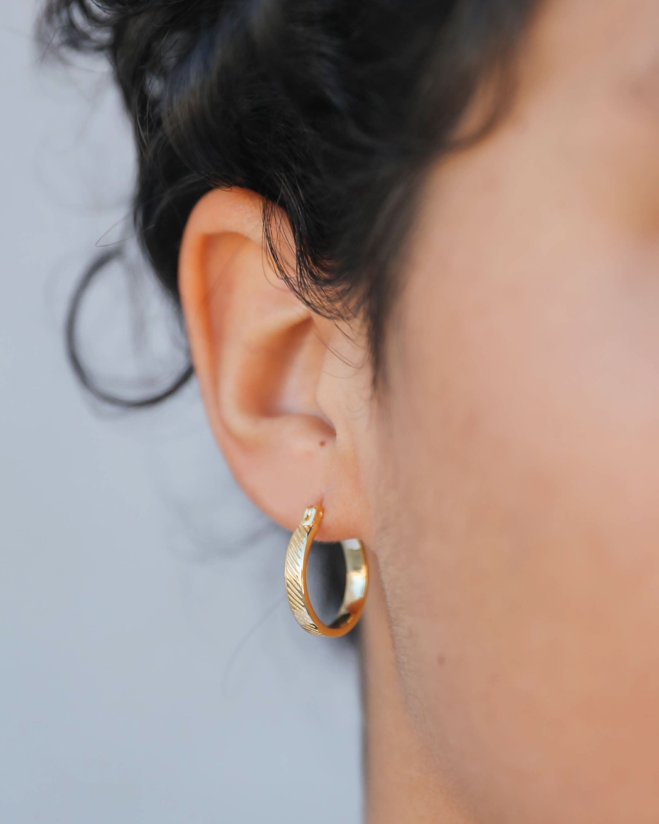 Gold hoop earring worn by a person with a blurred background