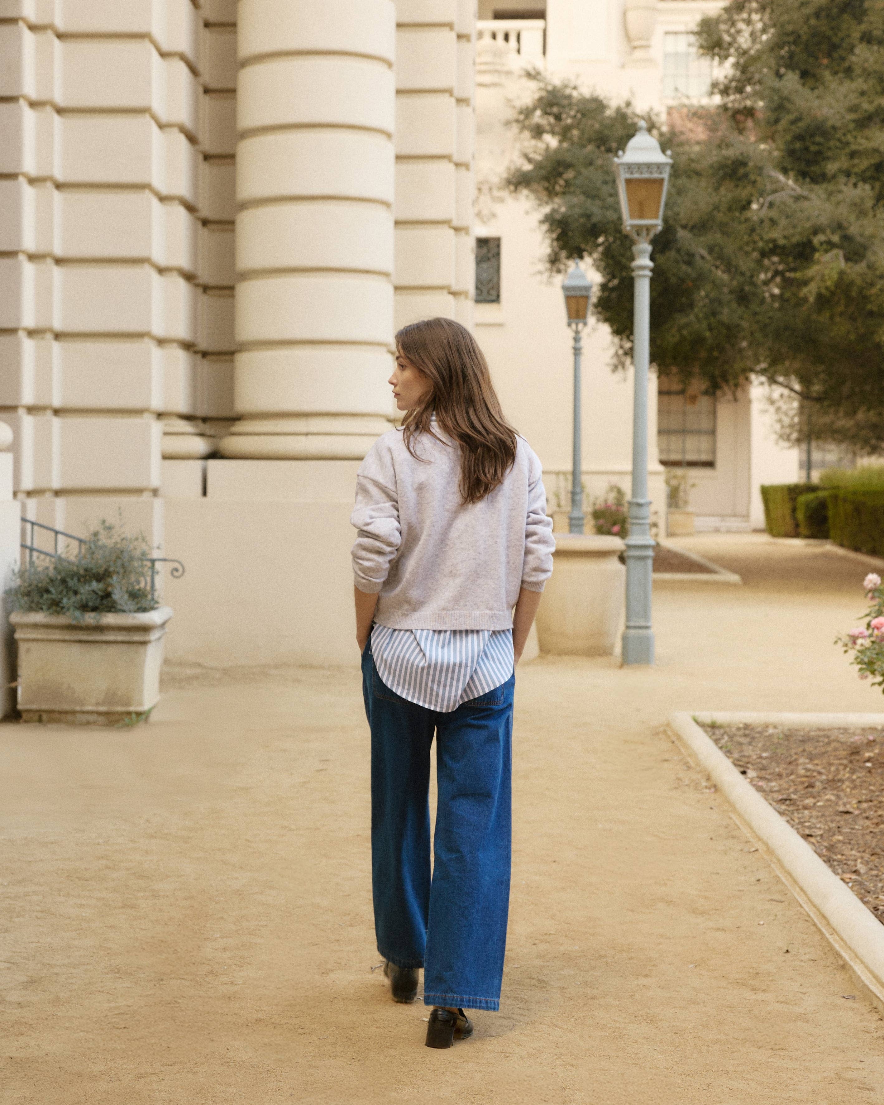 Woman walking on a sidewalk in an urban setting with a building and lamp