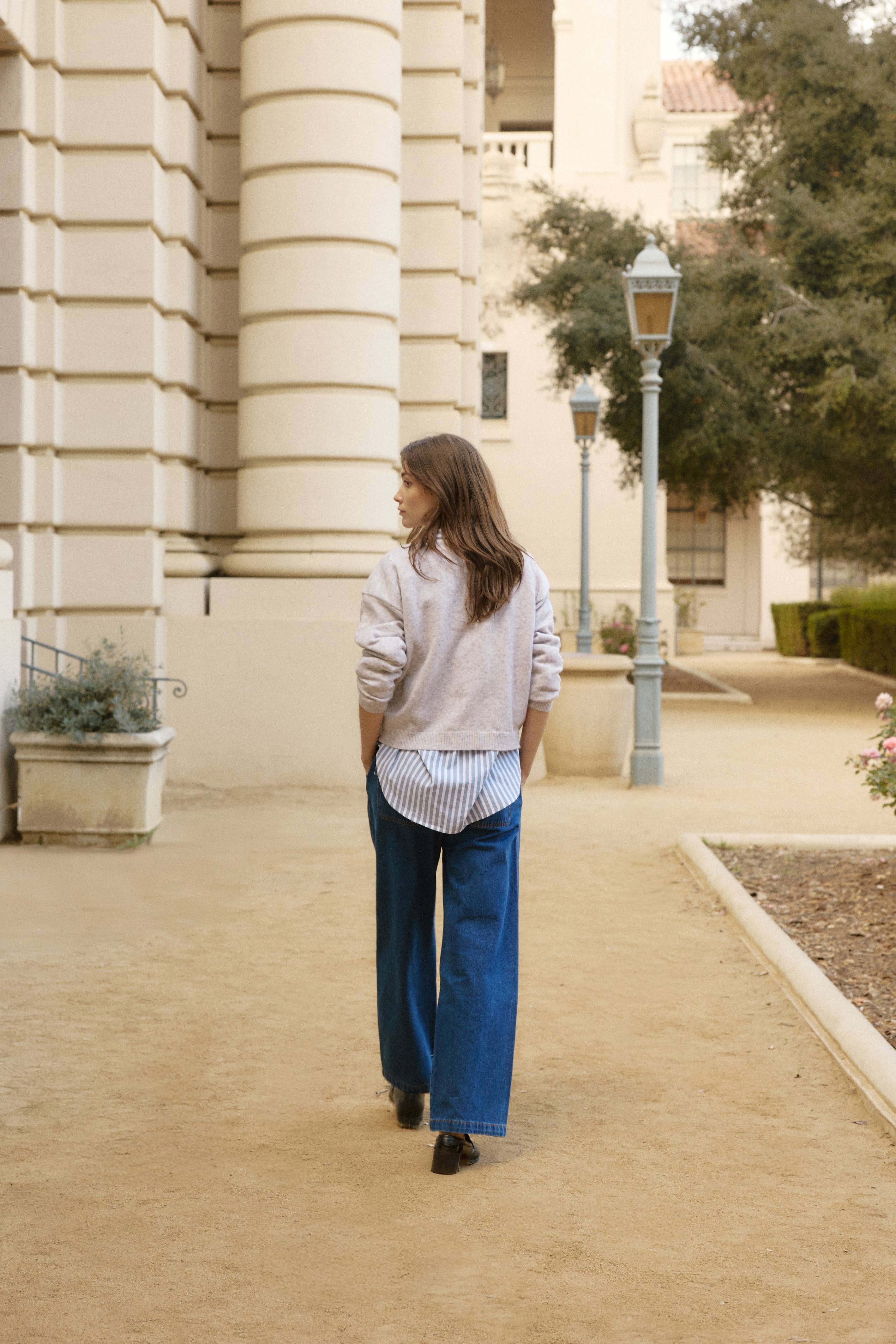 Woman walking on a sidewalk in an urban setting with a building and lamp
