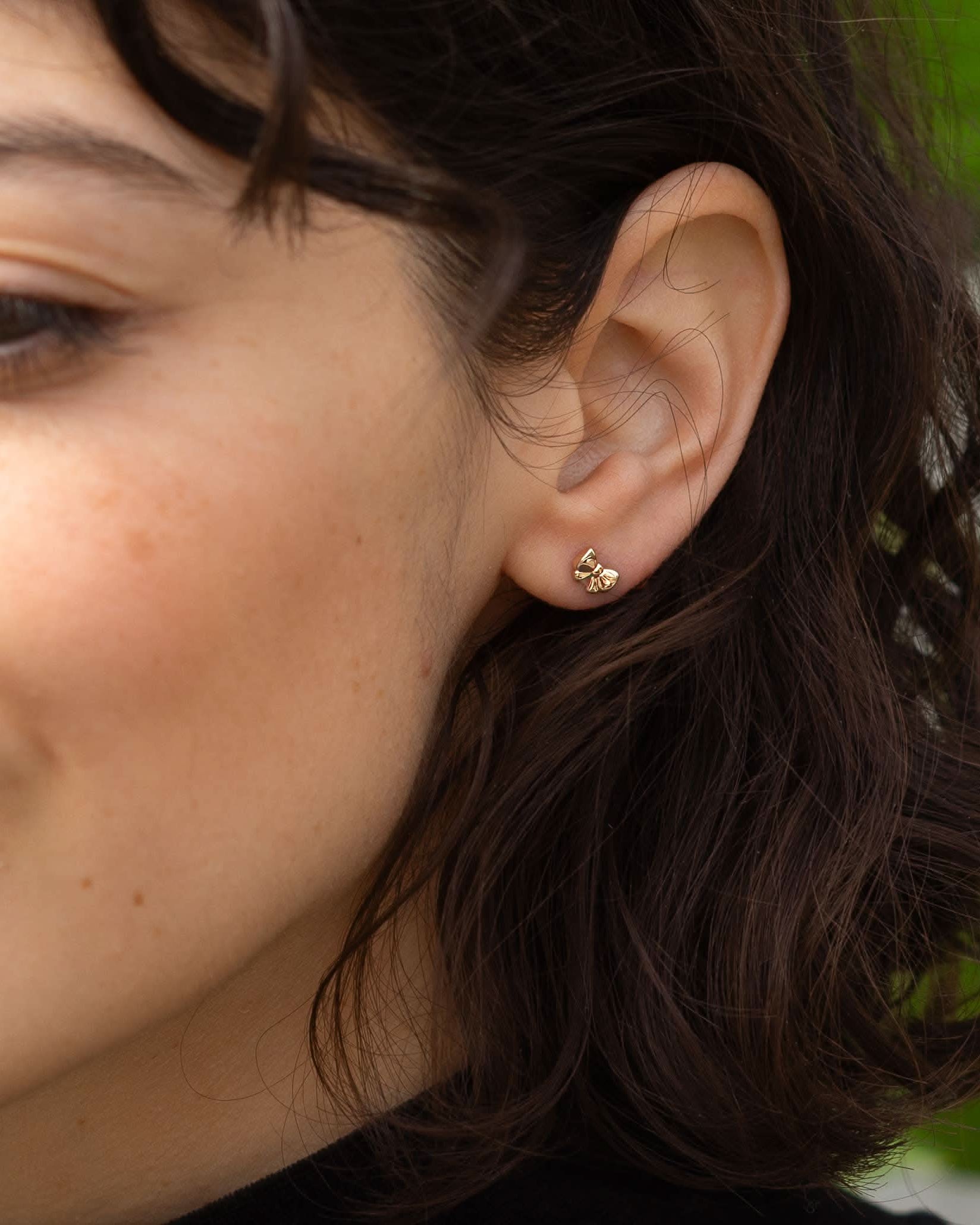 Close-up of a woman wearing gold earrings with a blurred green background