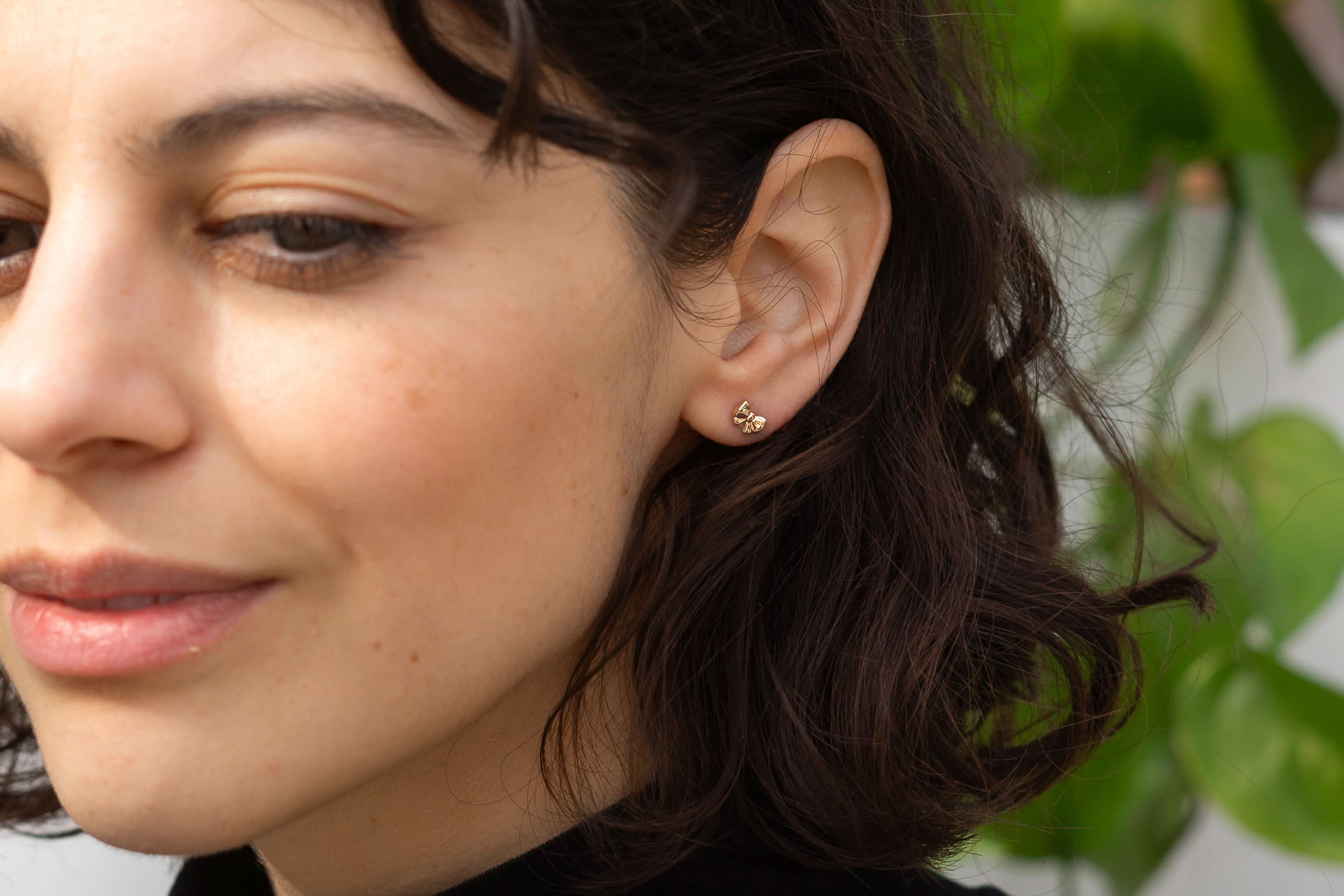 Close-up of a woman wearing gold earrings with a blurred green background