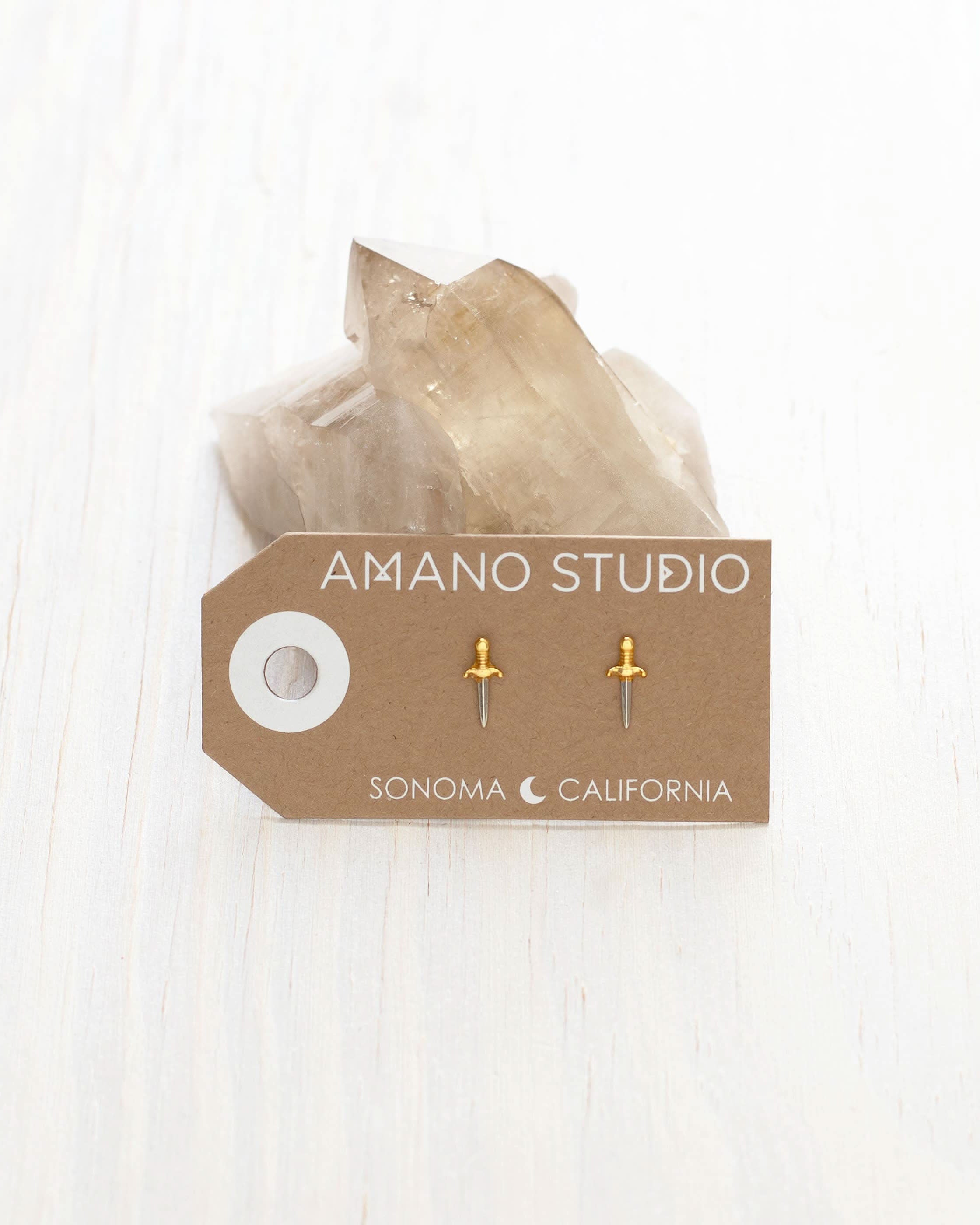 Tiny dagger stud earrings with gold handle and silver dagger shown on display card