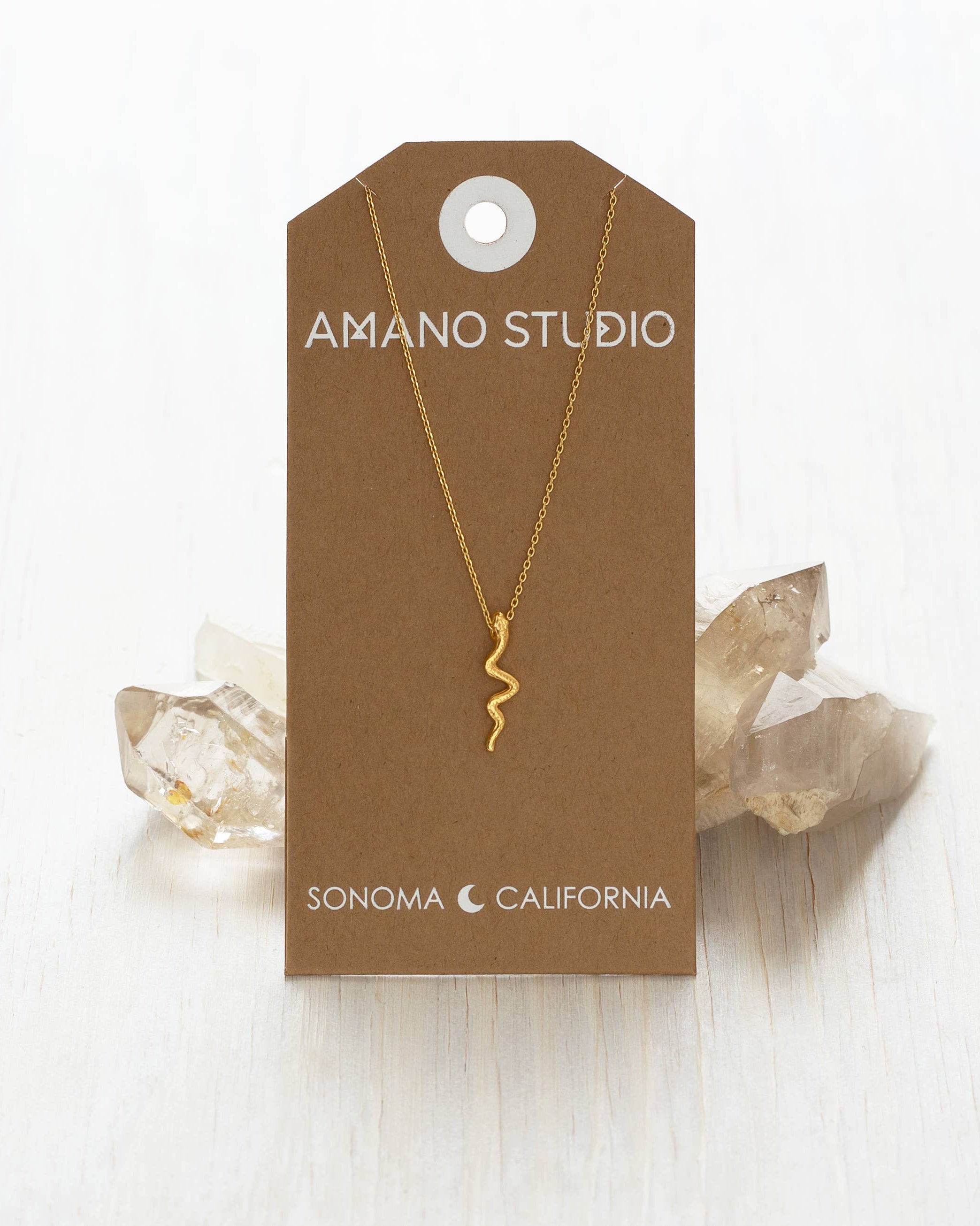 Gold necklace on a brown Amano Studio card with crystals in the background