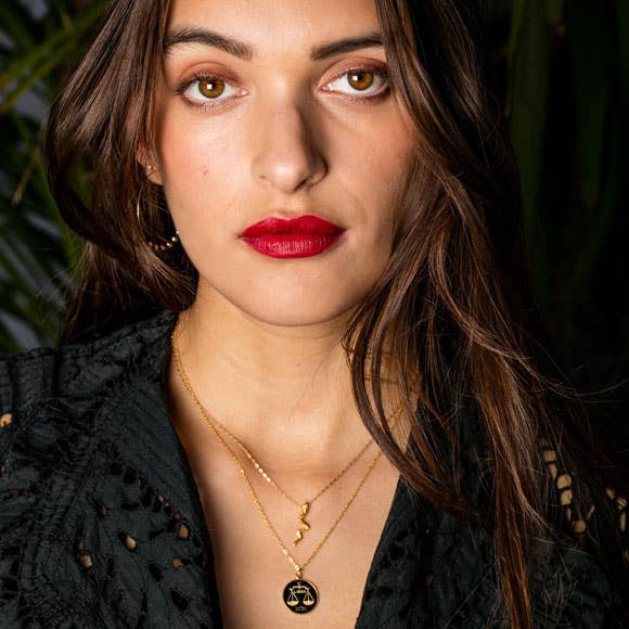 Woman wearing a black top and gold necklaces with a dark background