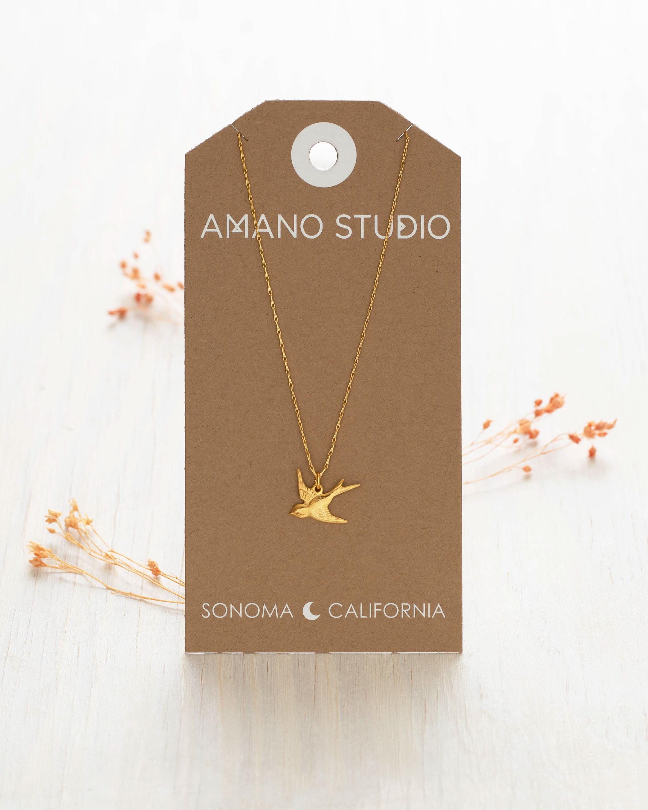 Gold bird necklace on a brown Amano Studio card