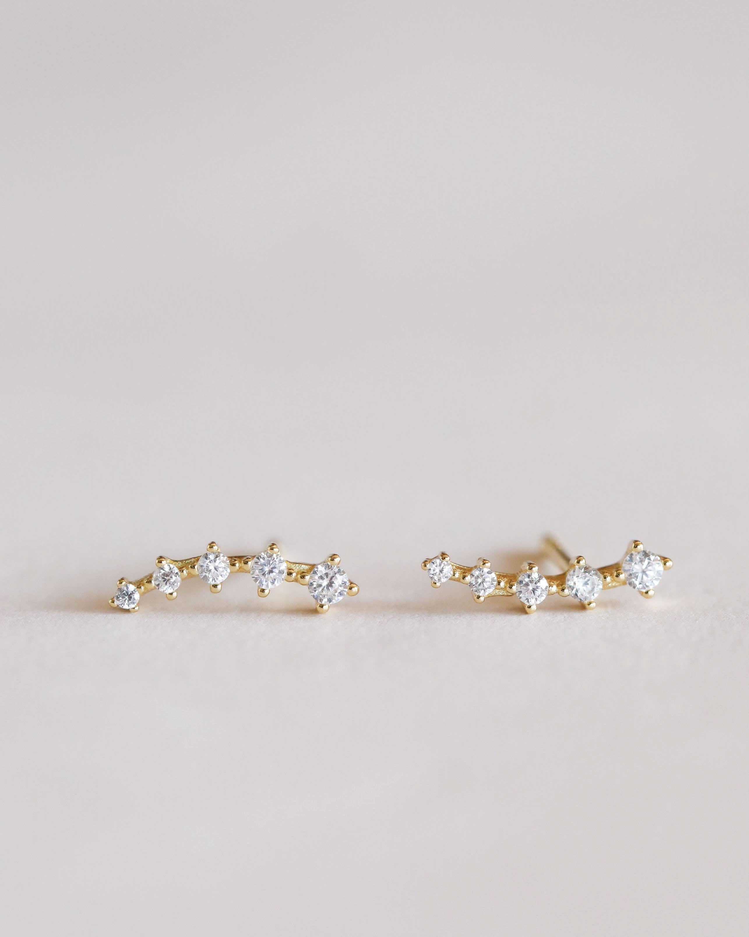 Pair of gold earrings with clear gemstones on a light pink background