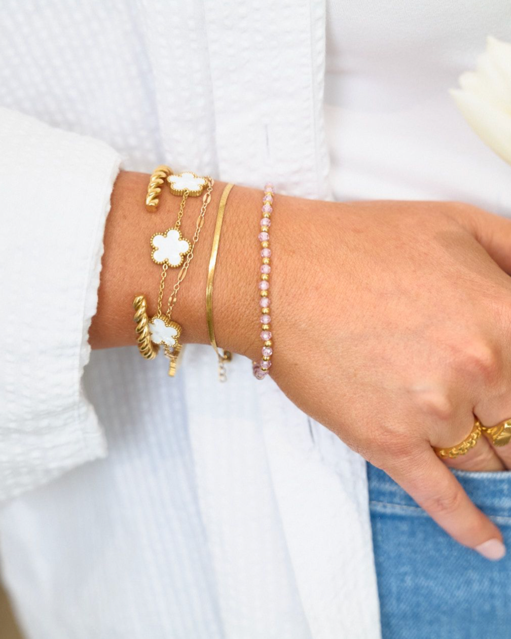 Hand wearing gold bracelets and a ring, holding a white tulip against