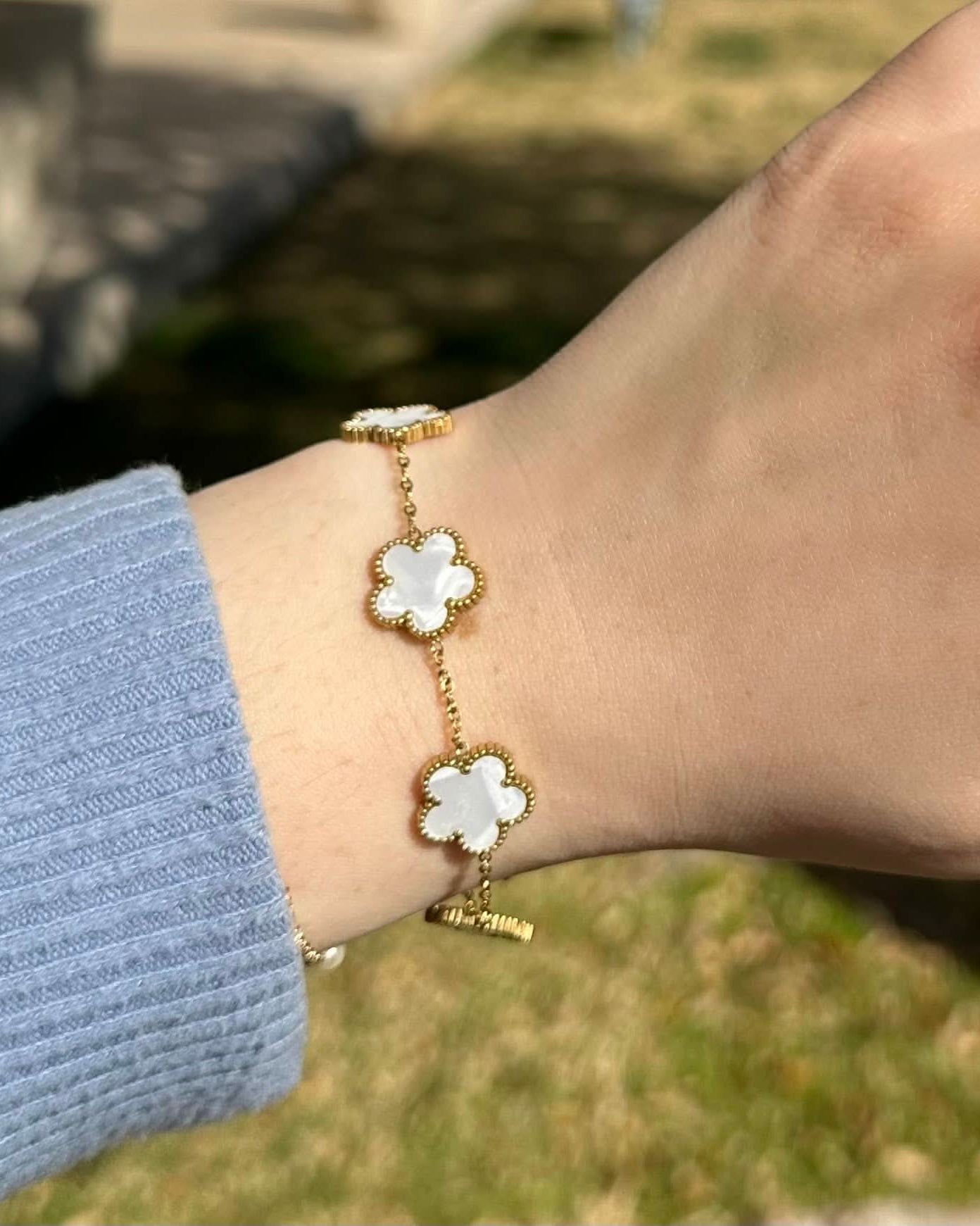 Gold bracelet with white flower charms on a wrist against a blurred