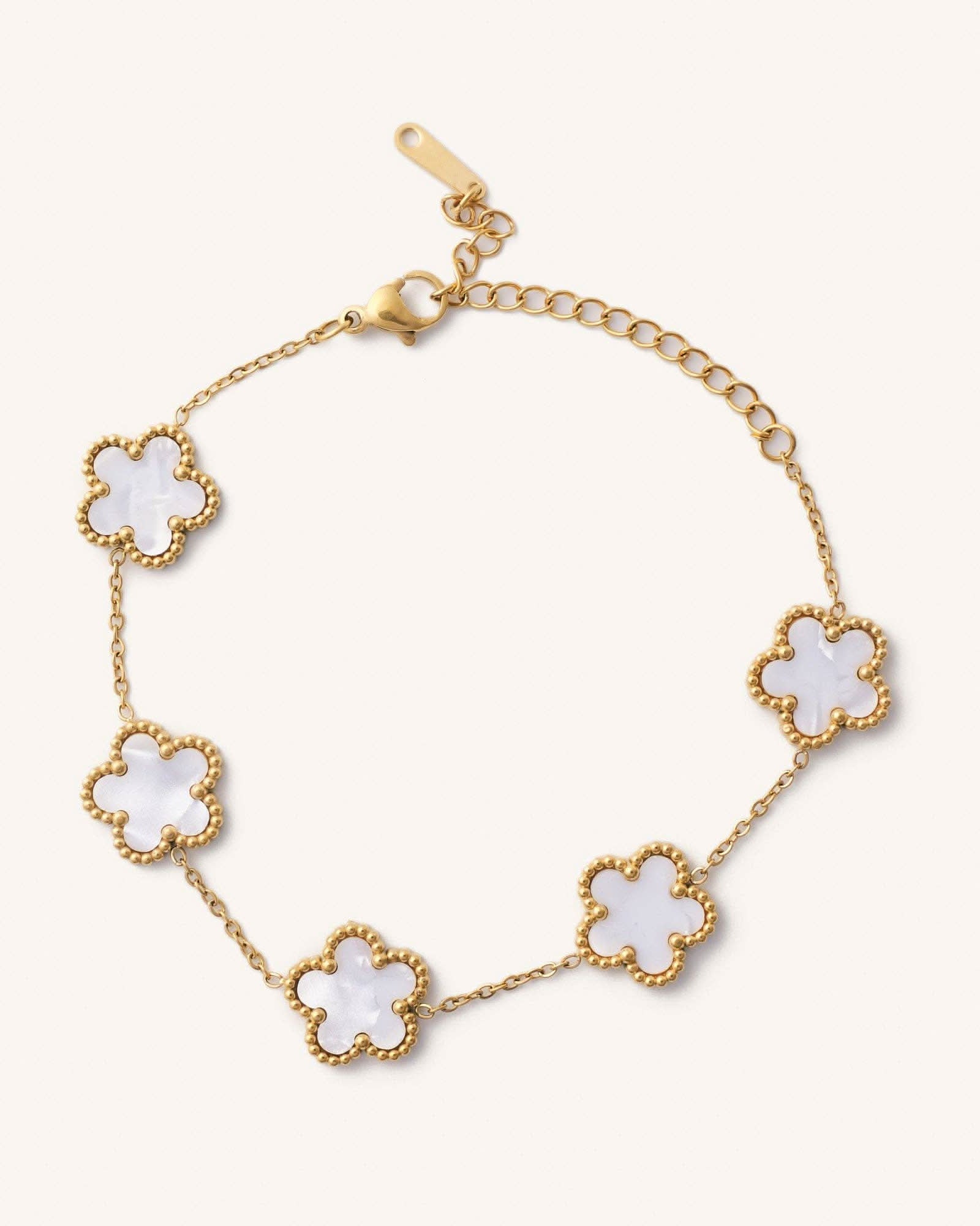 Gold bracelet with white flower-shaped charms on a light beige background