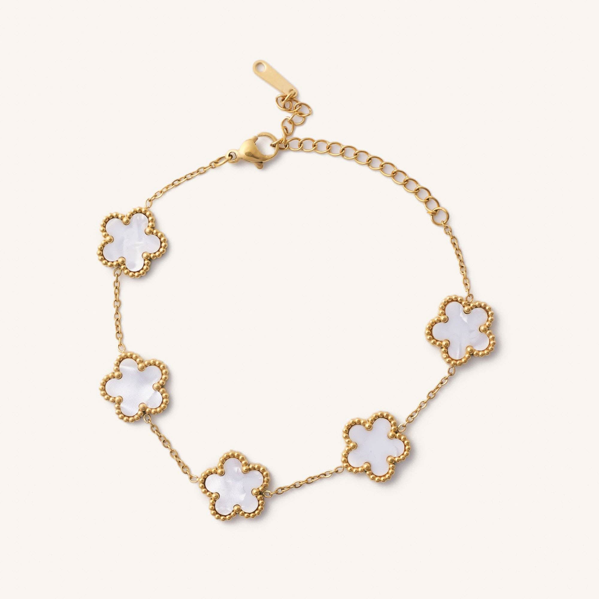 Gold bracelet with white flower-shaped charms on a light beige background