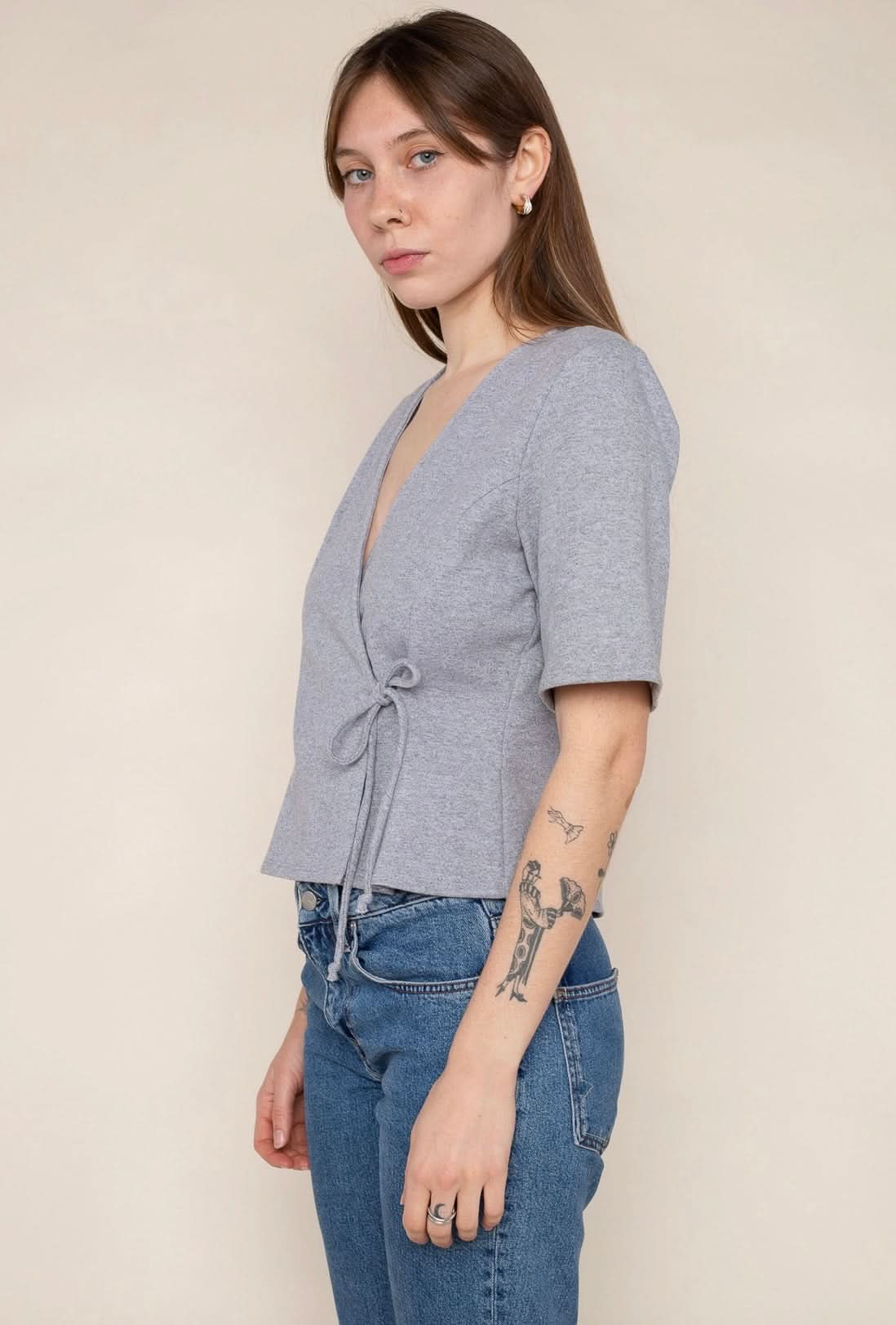 Woman wearing a grey wrap short sleeve shirt with blue jeans