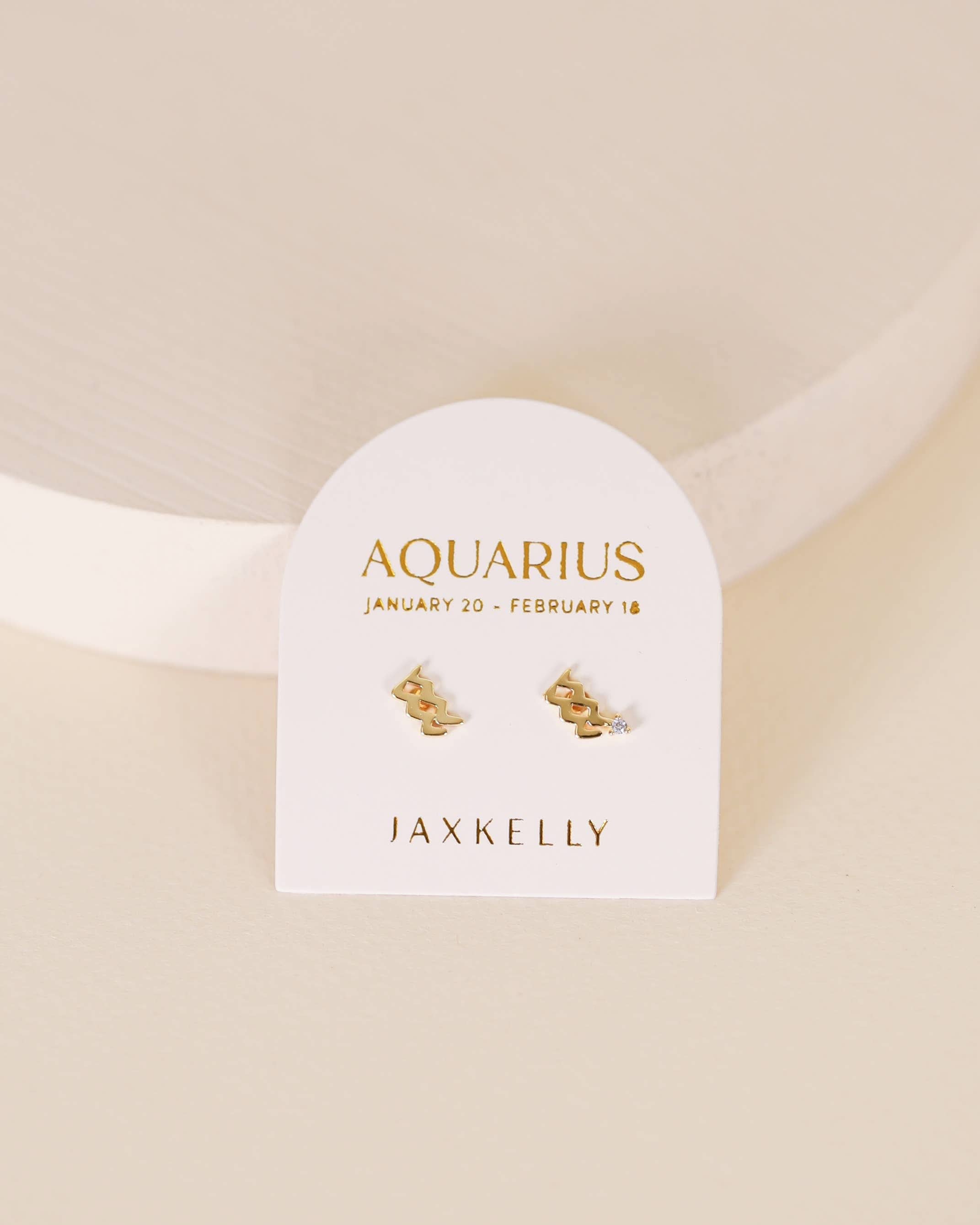 Gold zodiac charm studs in the shape of Aquarius astrological sign displayed on earring card