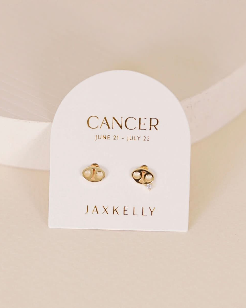 Gold zodiac charm studs in the shape of cancer astrological sign displayed on earring card