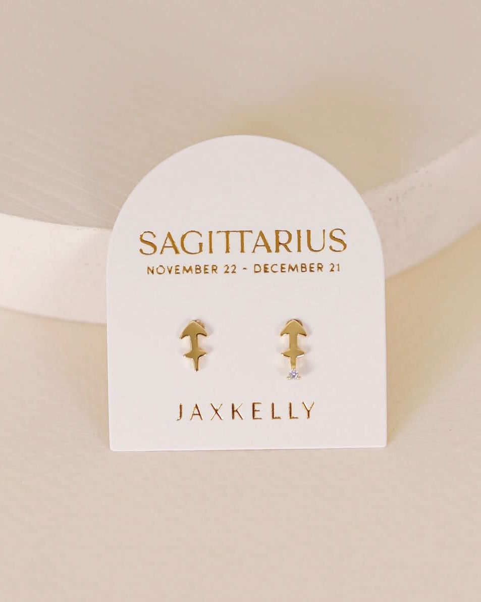 Gold zodiac charm studs in the shape of Sagittarius astrological sign displayed on earring card