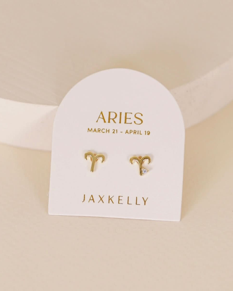 Gold zodiac charm studs in the shape of Aries astrological sign displayed on earring card