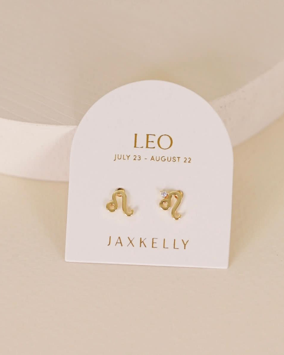 Gold zodiac charm studs in the shape of Leo astrological sign displayed on earring card