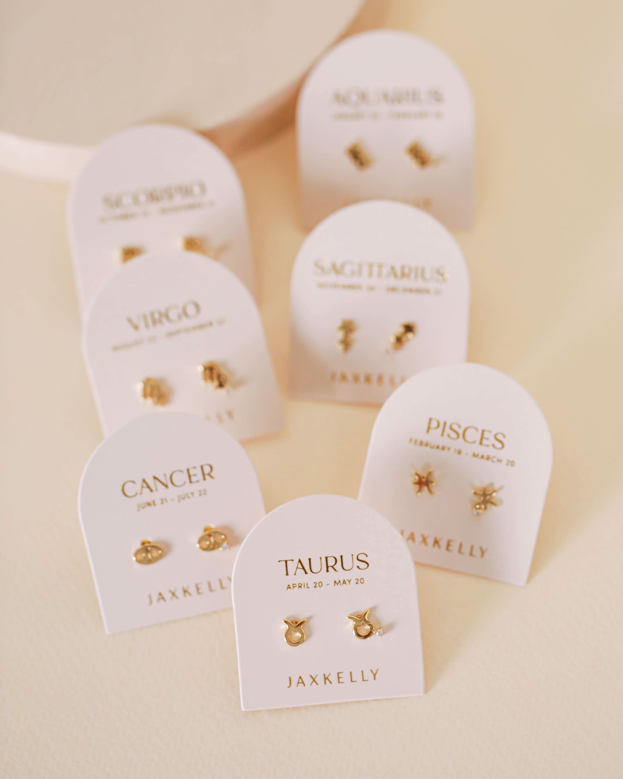Gold zodiac charm studs in the shape of Aquarius, Taurus, Pisces, Virgo, Scorpio.
