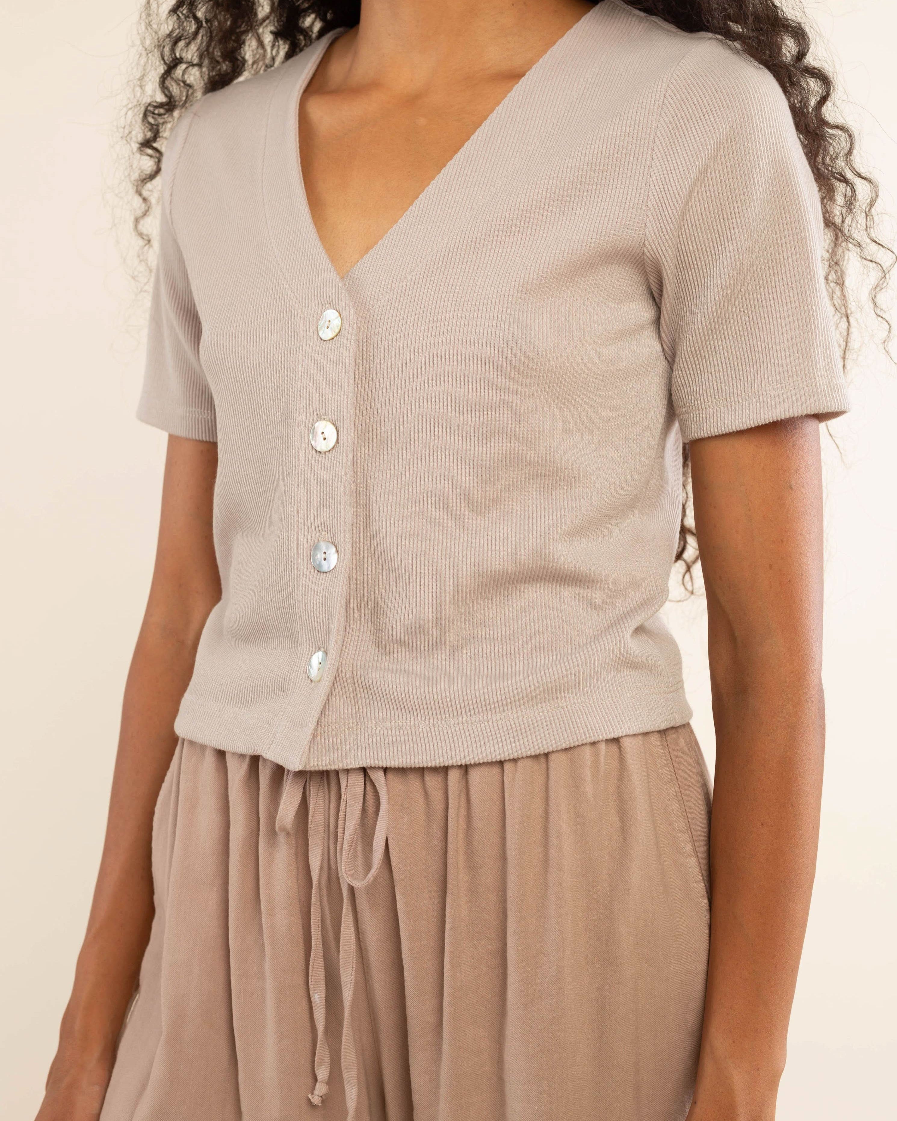 Woman wearing oat colored, ribbed, button down, short sleeve blouse top and beige pants