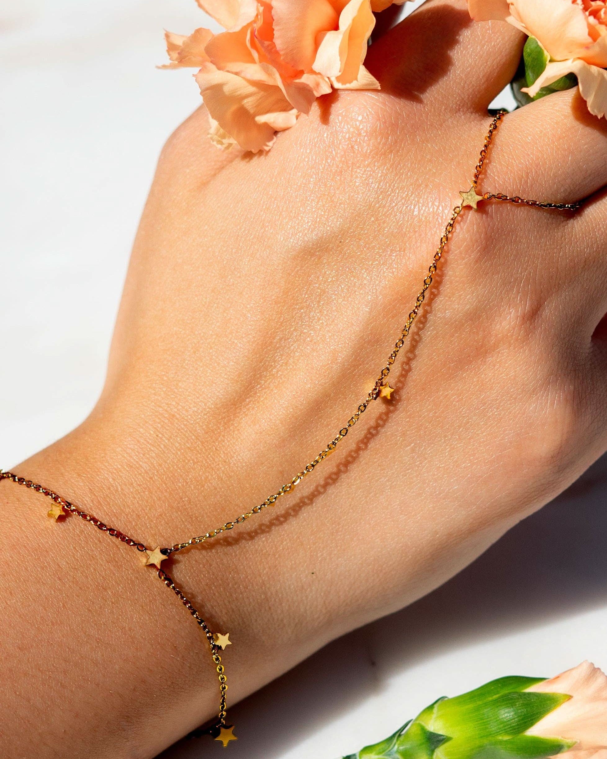 Hand wearing a delicate gold hand chain bracelet connected to a thin ring