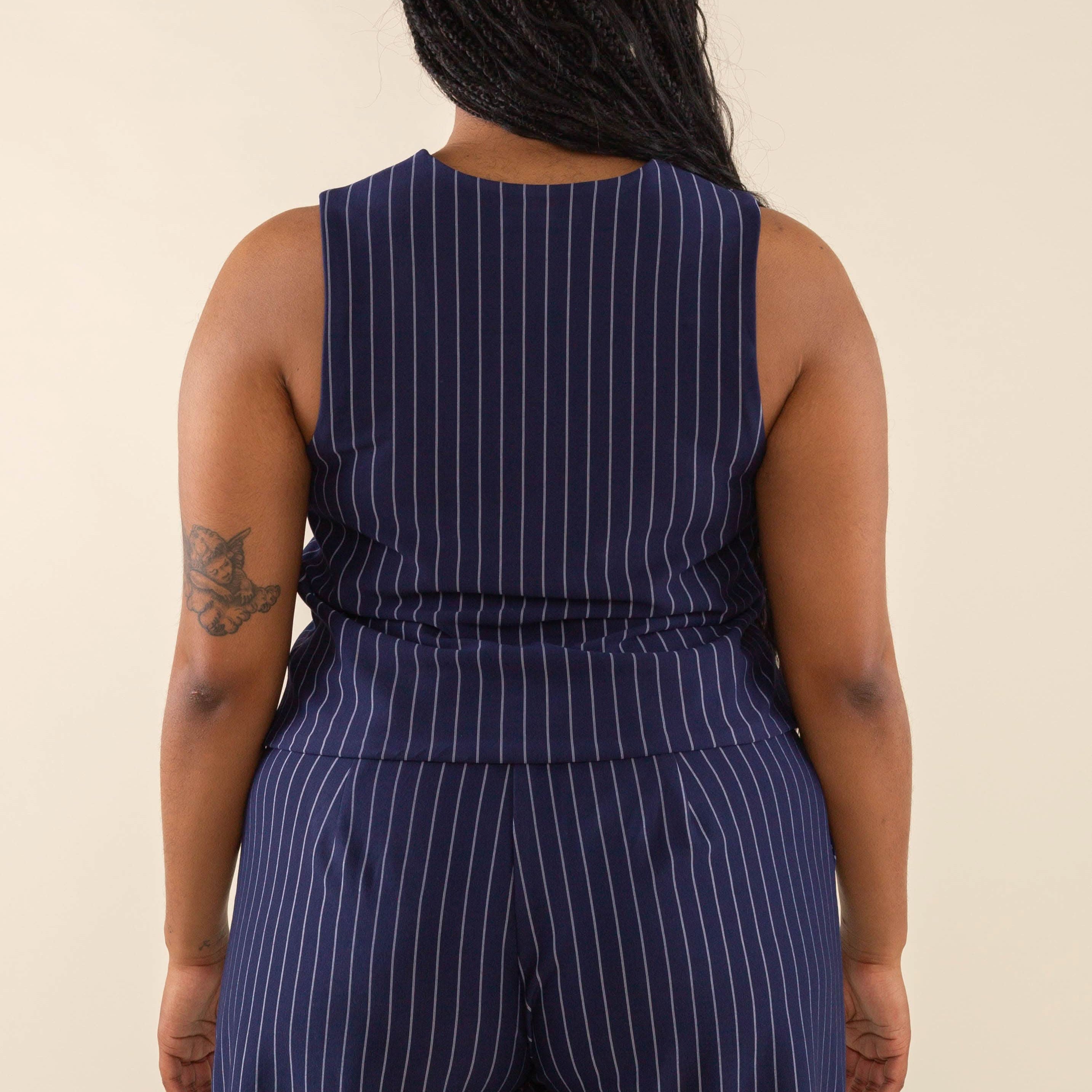 Woman facing away from the camera wearing navy blue high neck vest with cream pinstripes. Vest has navy blue buttons all the way down