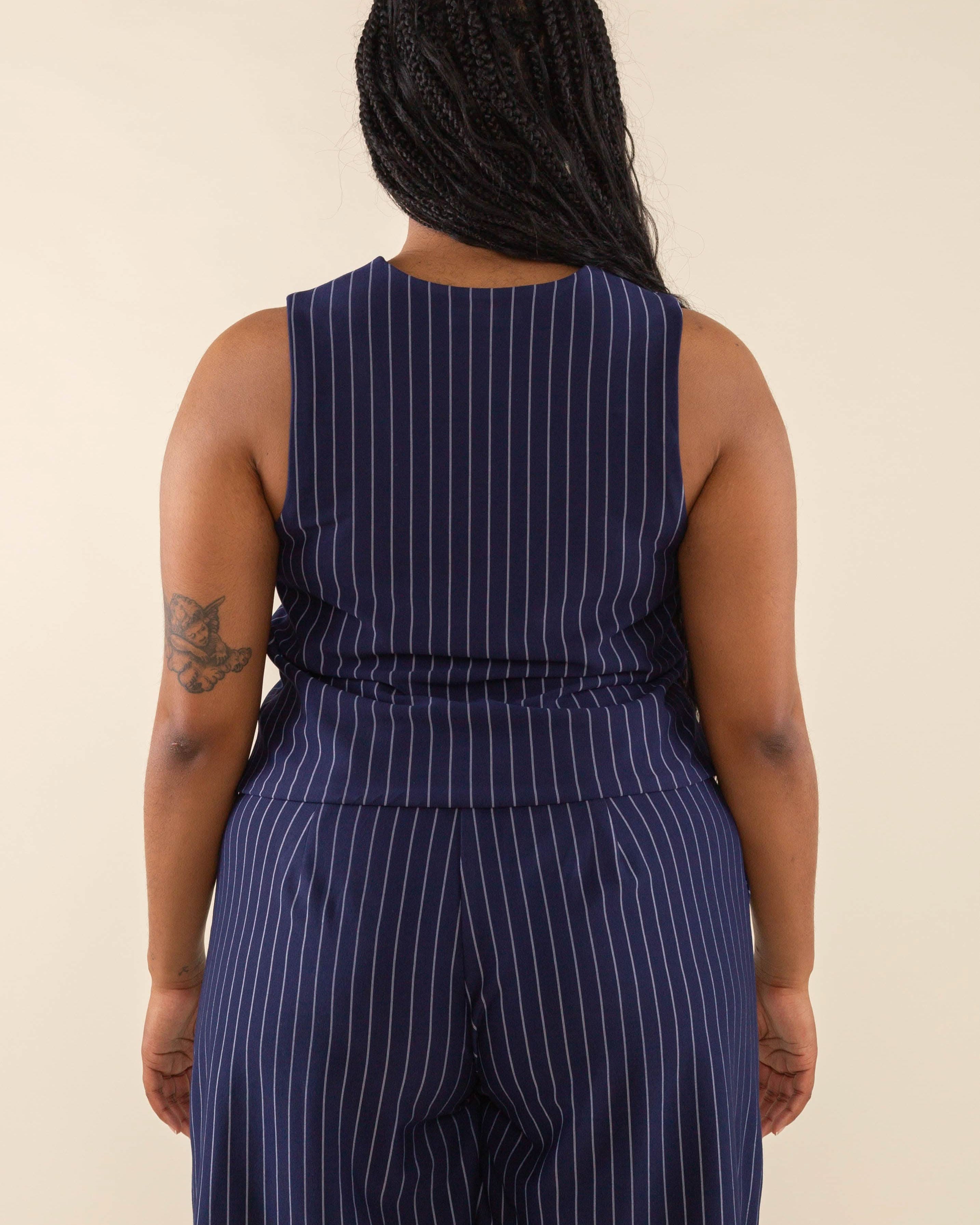 Woman facing away from the camera wearing navy blue high neck vest with cream pinstripes. Vest has navy blue buttons all the way down