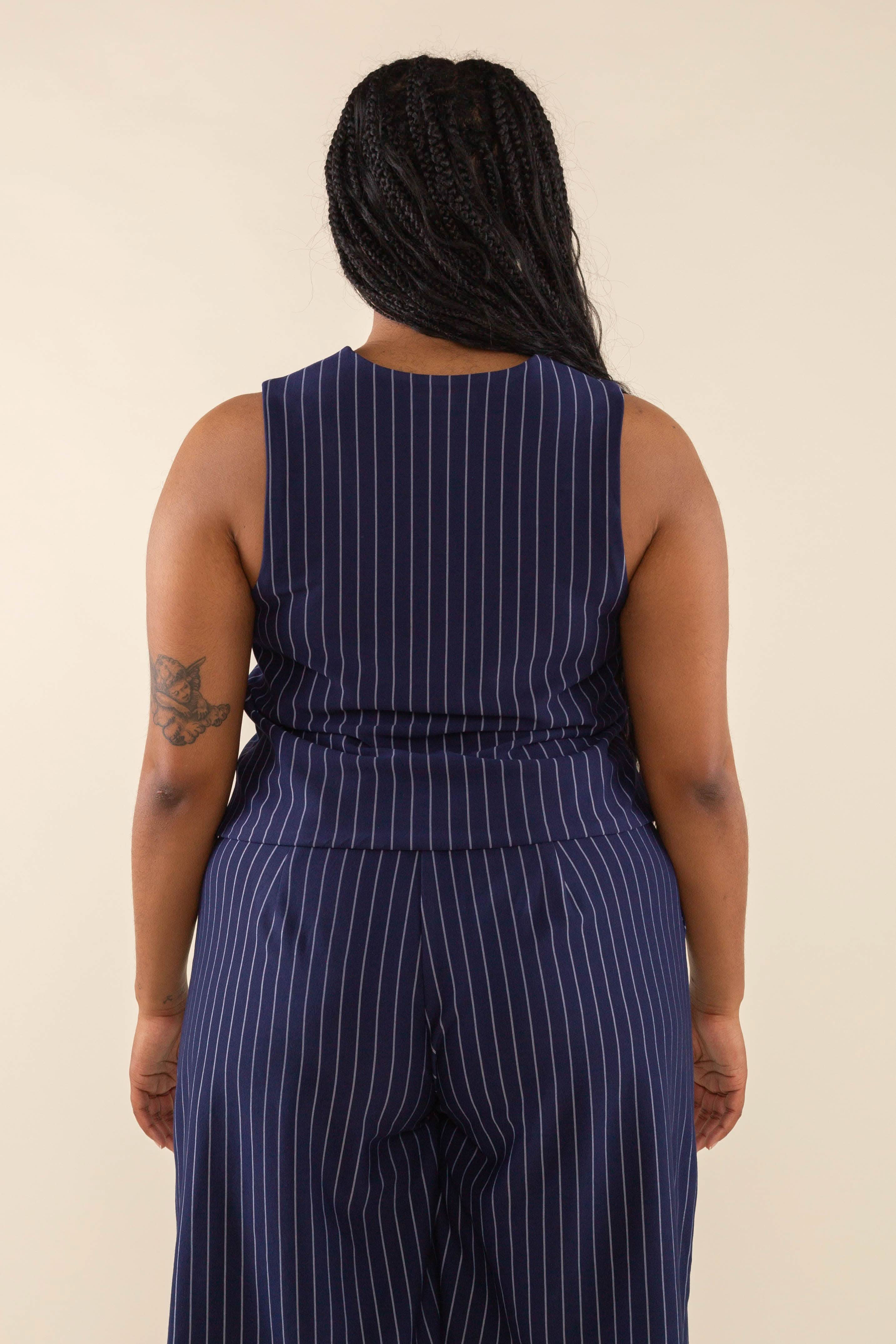 Woman facing away from the camera wearing navy blue high neck vest with cream pinstripes. Vest has navy blue buttons all the way down