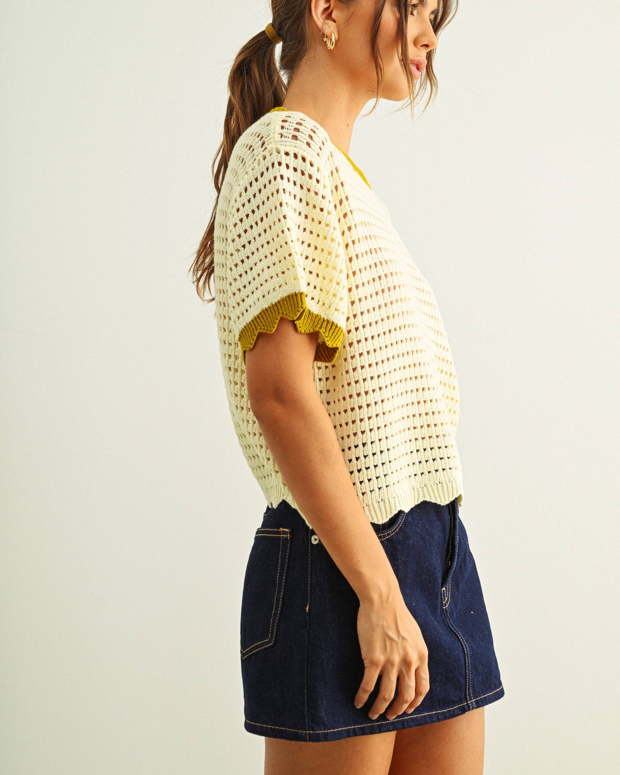 Woman wearing a white crochet top and denim skirt on a plain background