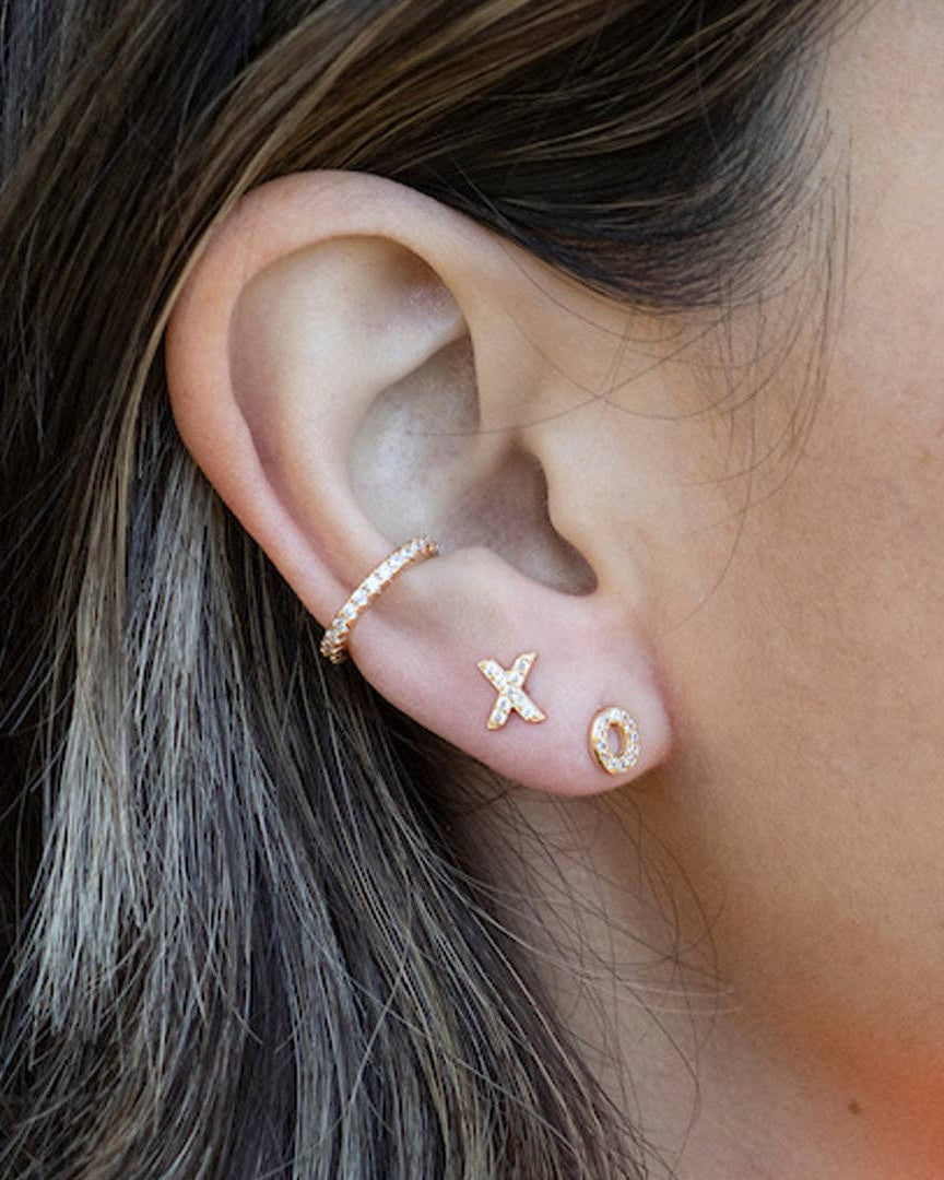 Close-up of an ear wearing gold earrings with 'XO' design.