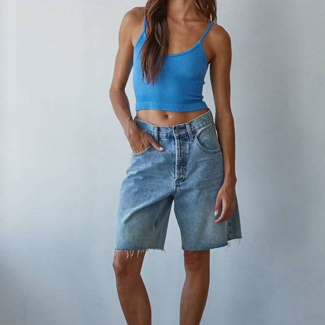 Woman wearing a blue tank top and denim shorts against a plain background