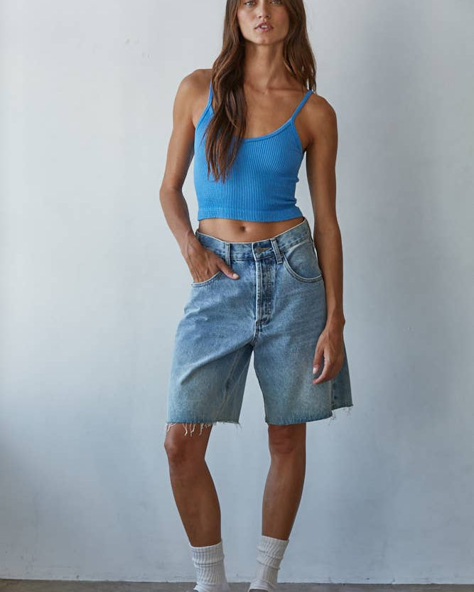 Woman wearing a blue tank top and denim shorts against a plain background