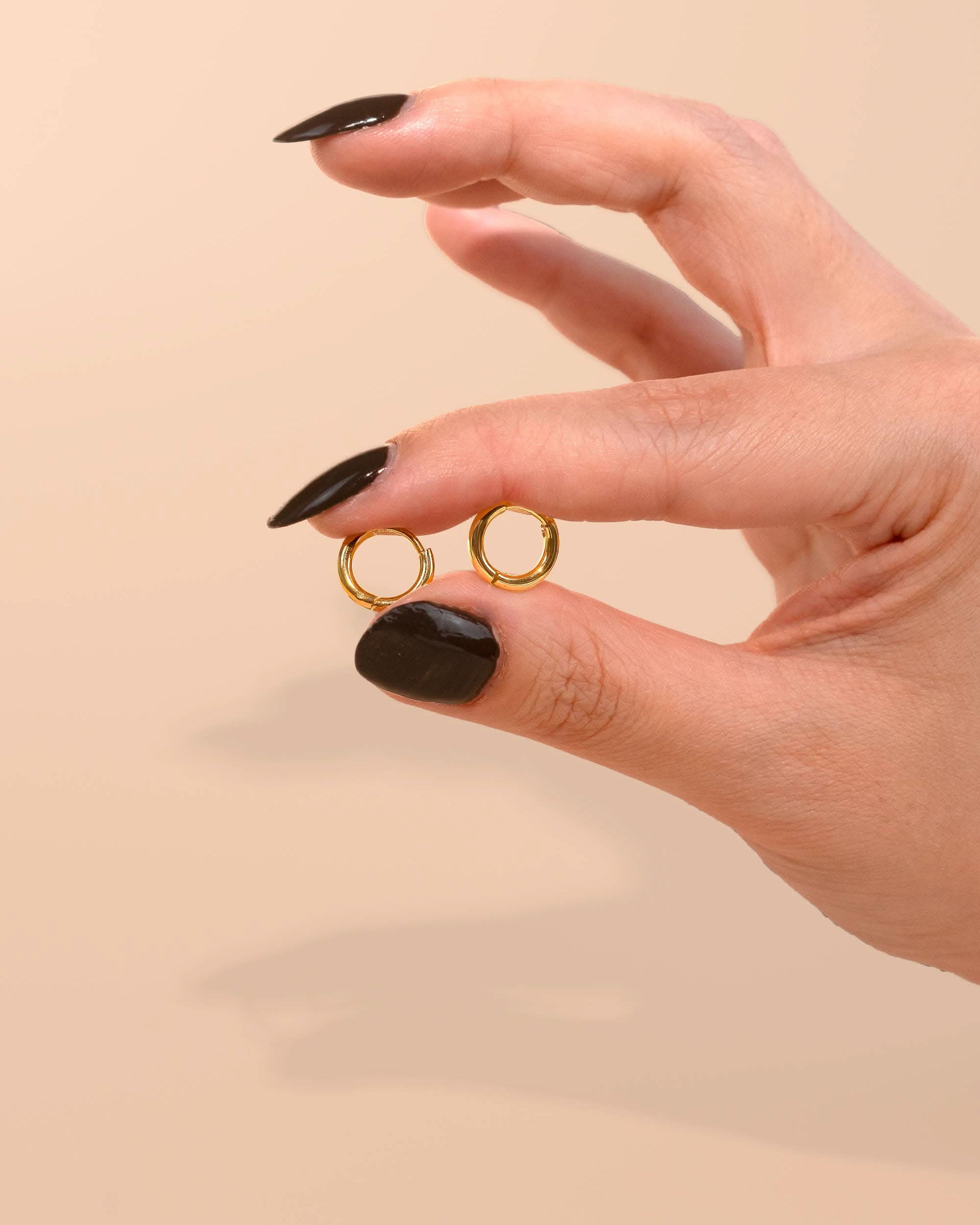 Woman holding the everyday gold Huggies medium sized hoops on a pink peach background