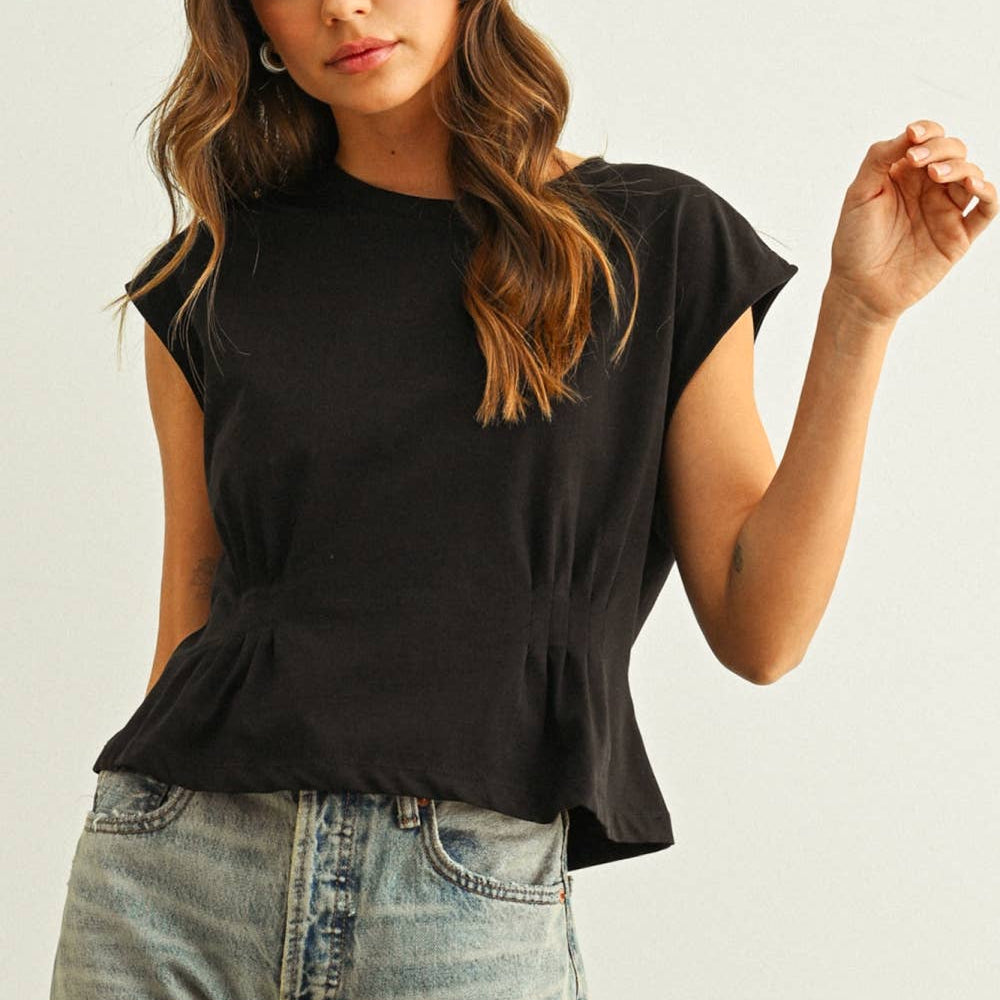 Woman wearing a black top and light blue jeans against a plain background