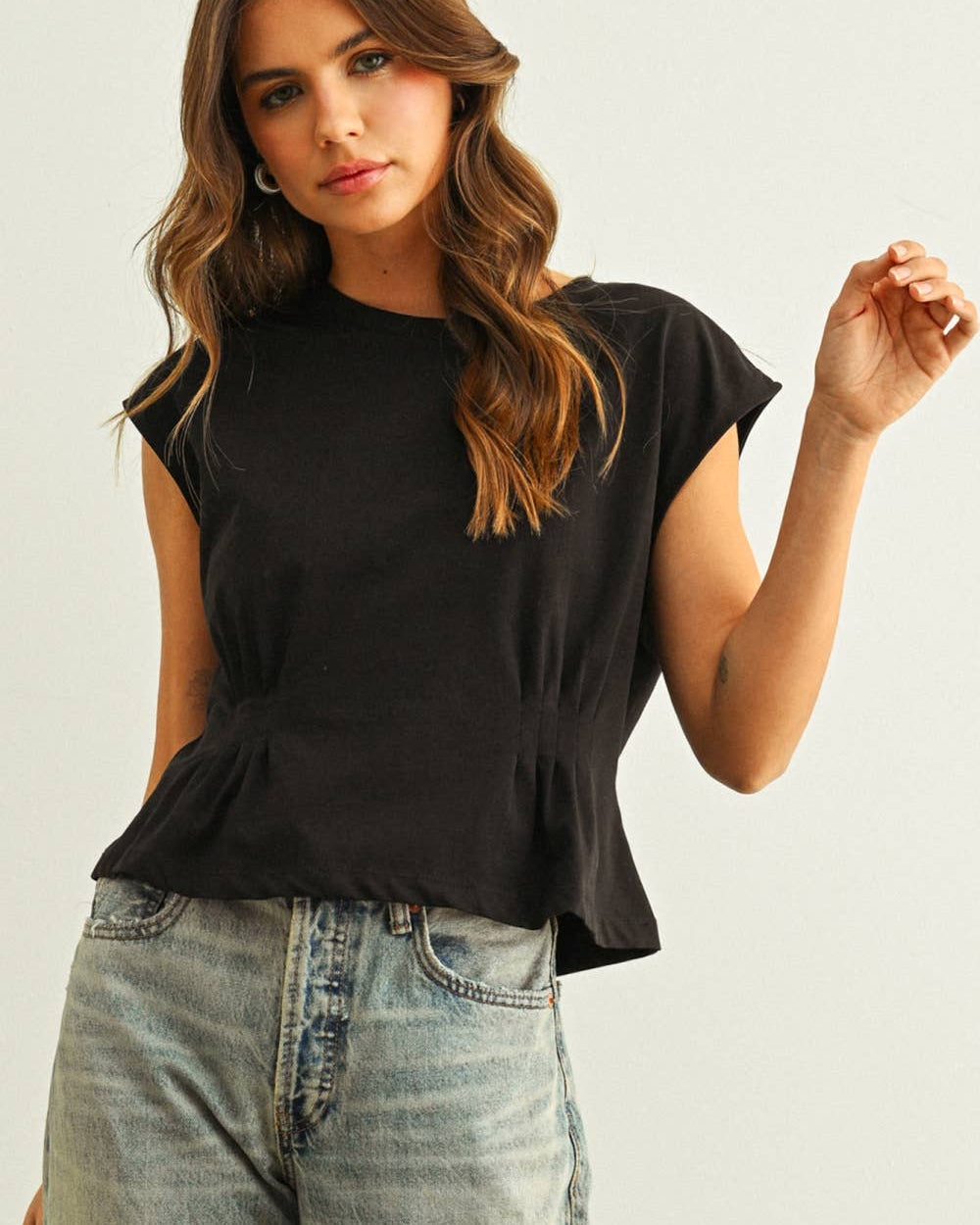 Woman wearing a black top and light blue jeans against a plain background