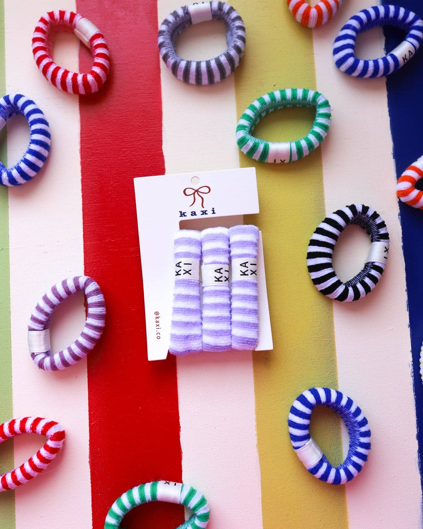 Colorful hair ties on a multicolored striped background with Kazi packaging.