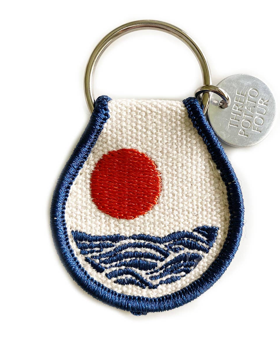 Keychain with embroidered design of a red circle and blue waves on a white background