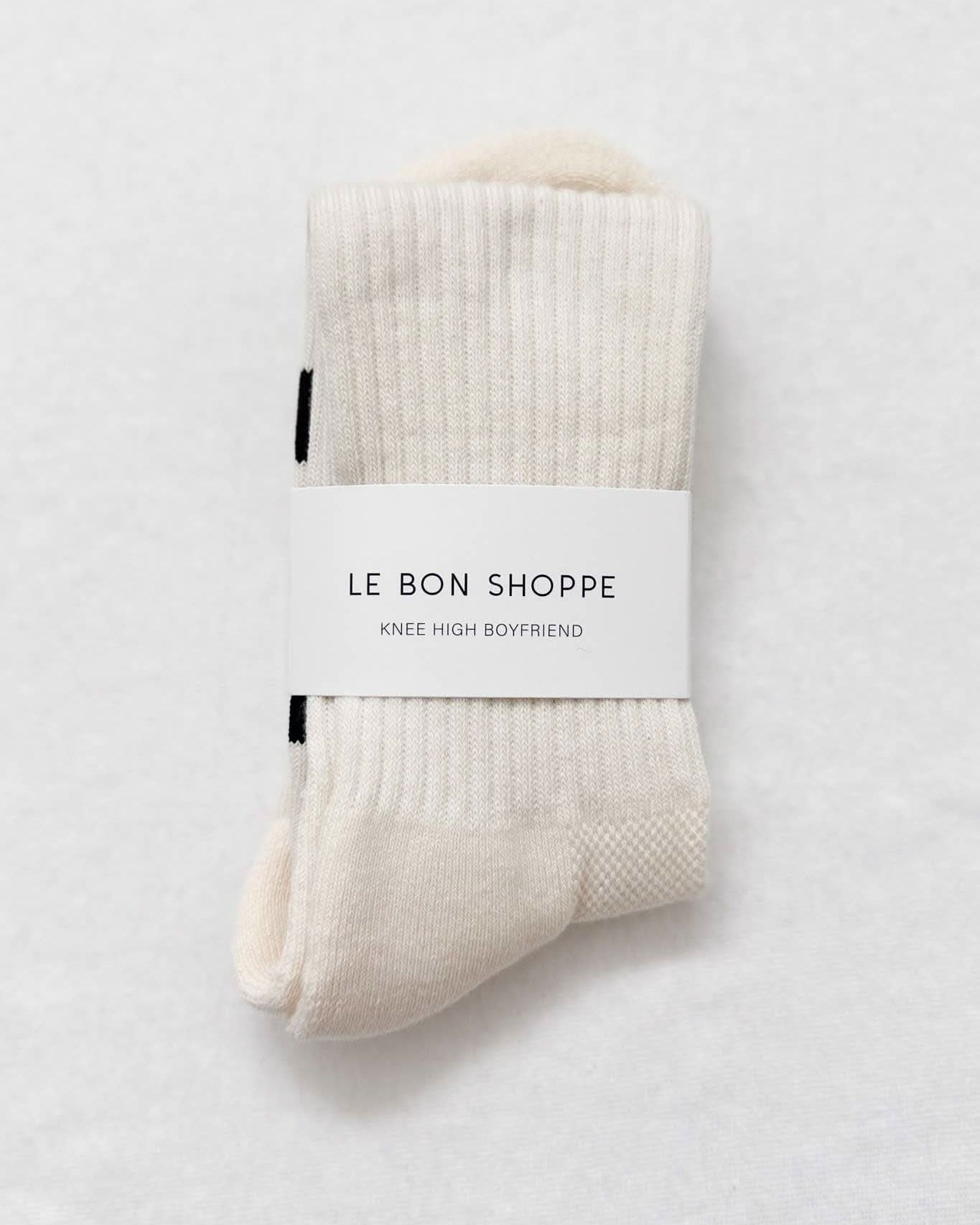 Pair of beige knee-high socks with 'Le Bon Shoppe' label on a light gray background