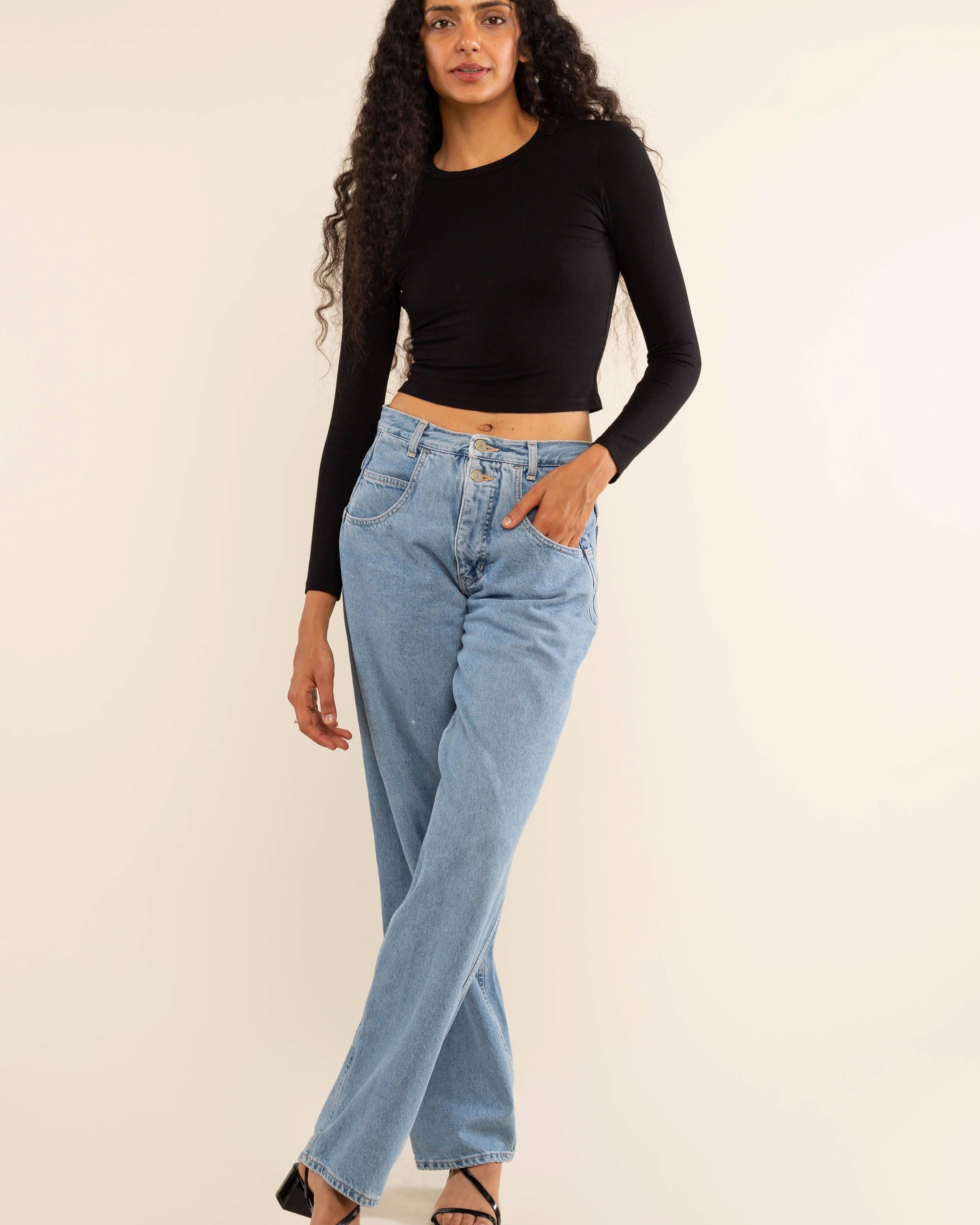 Woman wearing white, long sleeve, tight, crew neck, top with blue jeans
