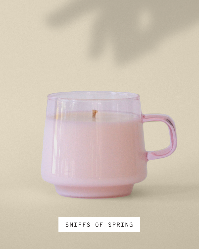 Candle in pink opaque reusable, stackable mug sitting in the sun against a cream colored wall