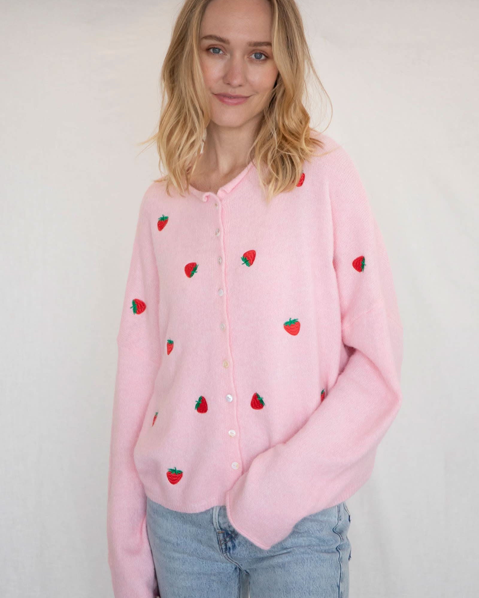 Woman wearing a pink button down cardigan with strawberries and blue jeans