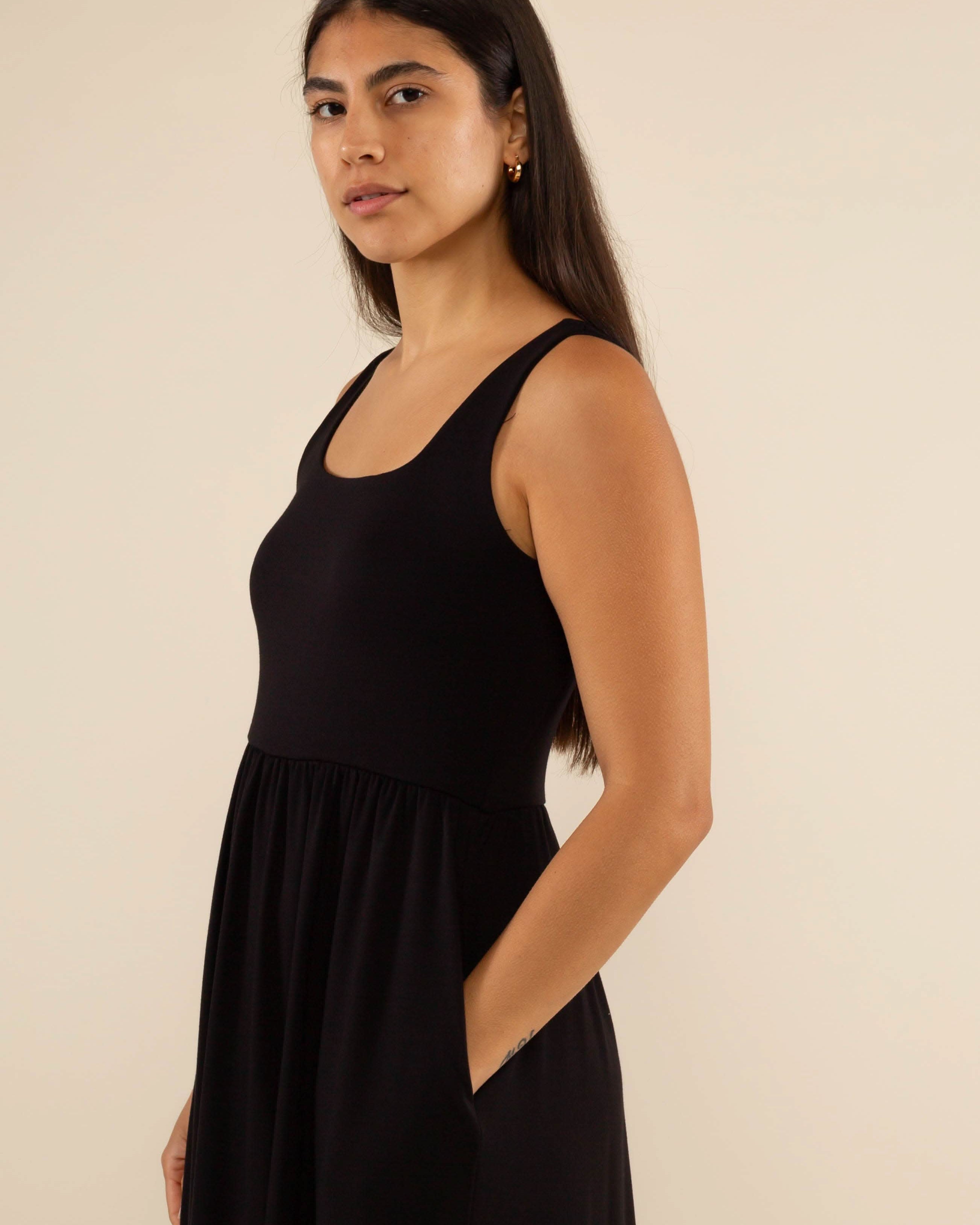 Woman wearing a black sleeveless dress against a beige background