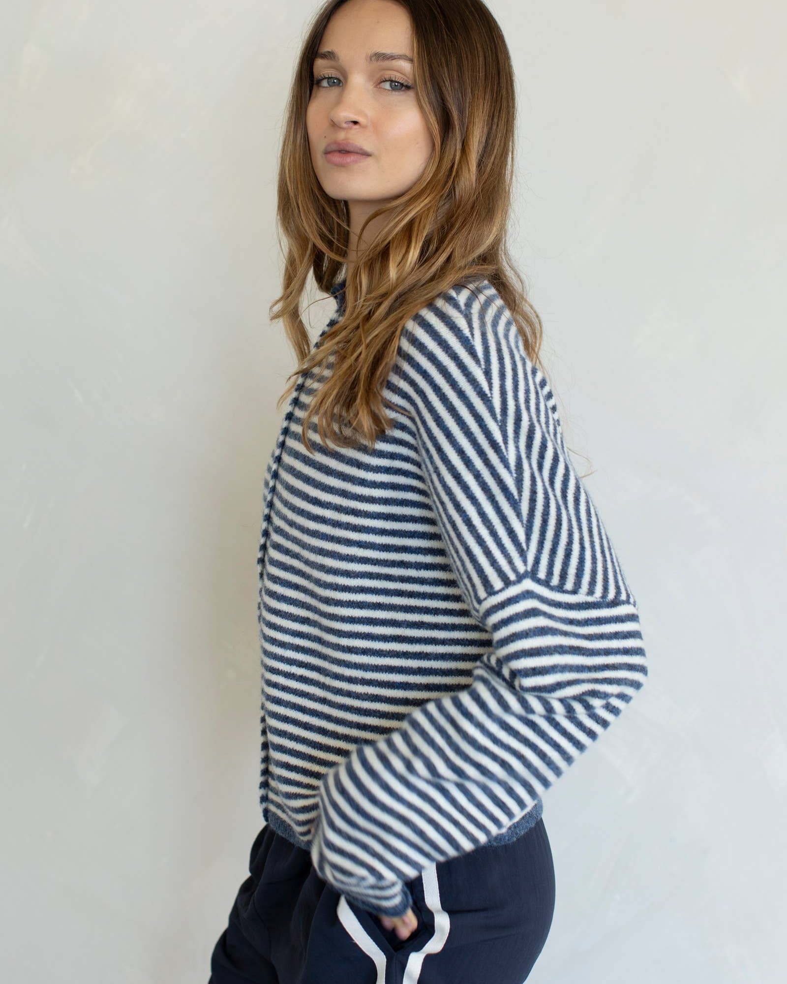 Woman wearing a striped sweater and dark pants against a plain background
