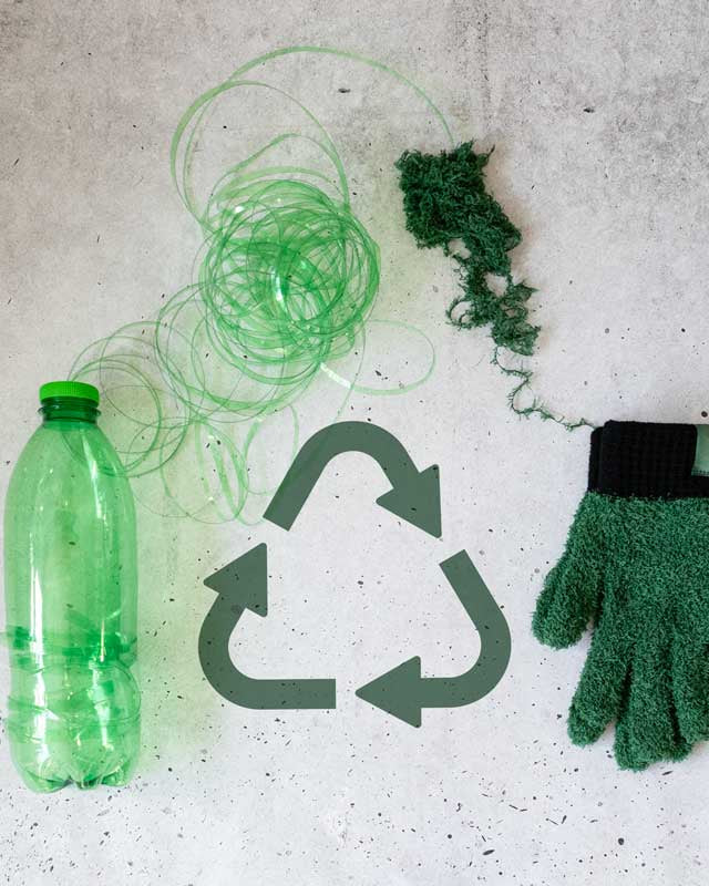 Recycling theme with green bottle, gloves, and yarn on a concrete surface.