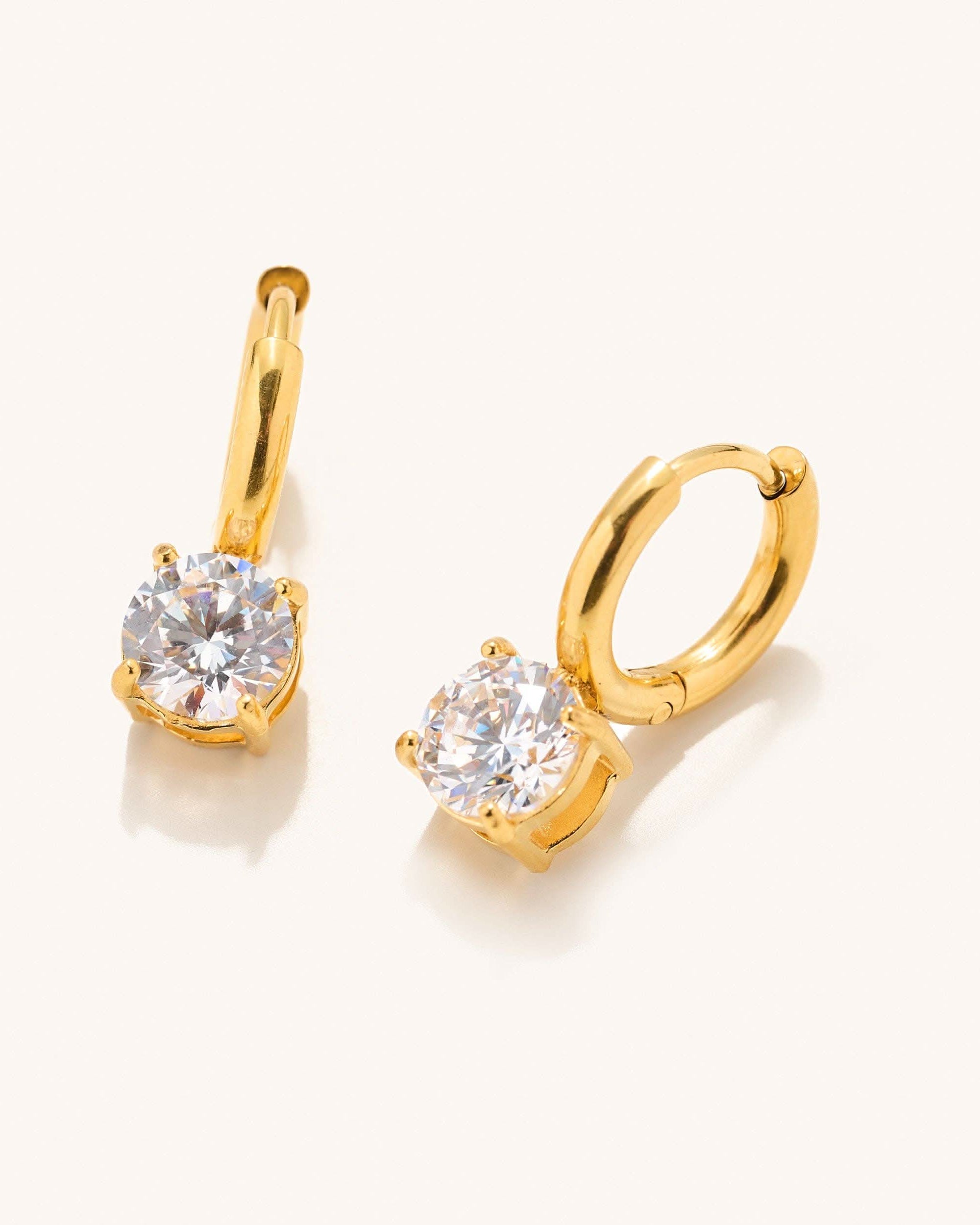 Gold huggie earrings with gem dangle detail laying on a white backdrop