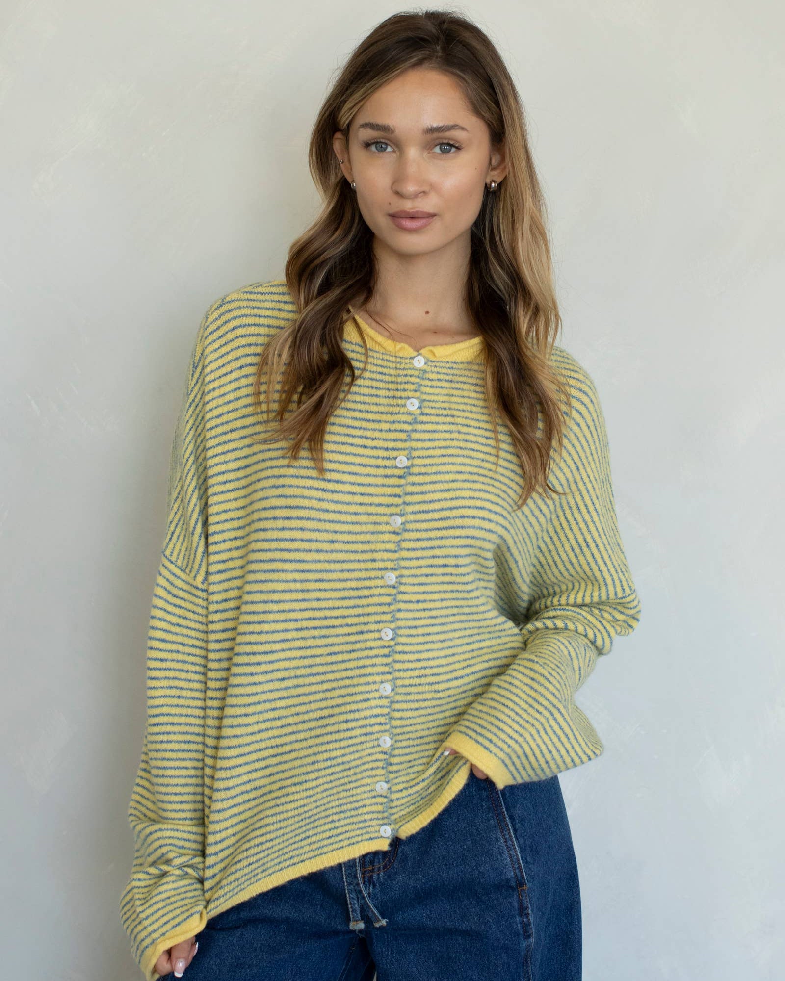 Woman wearing a yellow striped shirt and blue jeans against a plain background